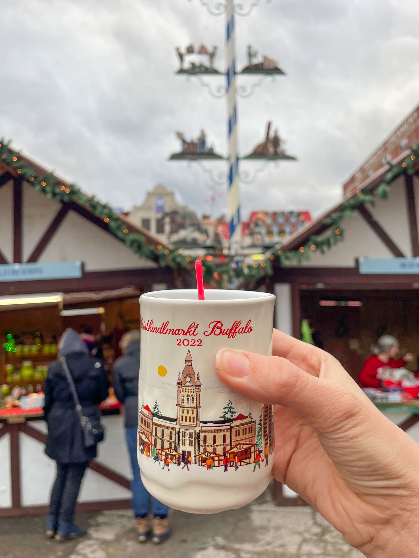 Holding up a mug that reads 'Christkindlmarket Buffalo 2022' inside the Buffalo Holiday Market.