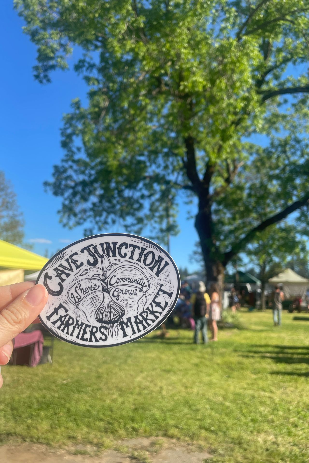 Holding up a sticker that reads Cave Junction Farmers Market