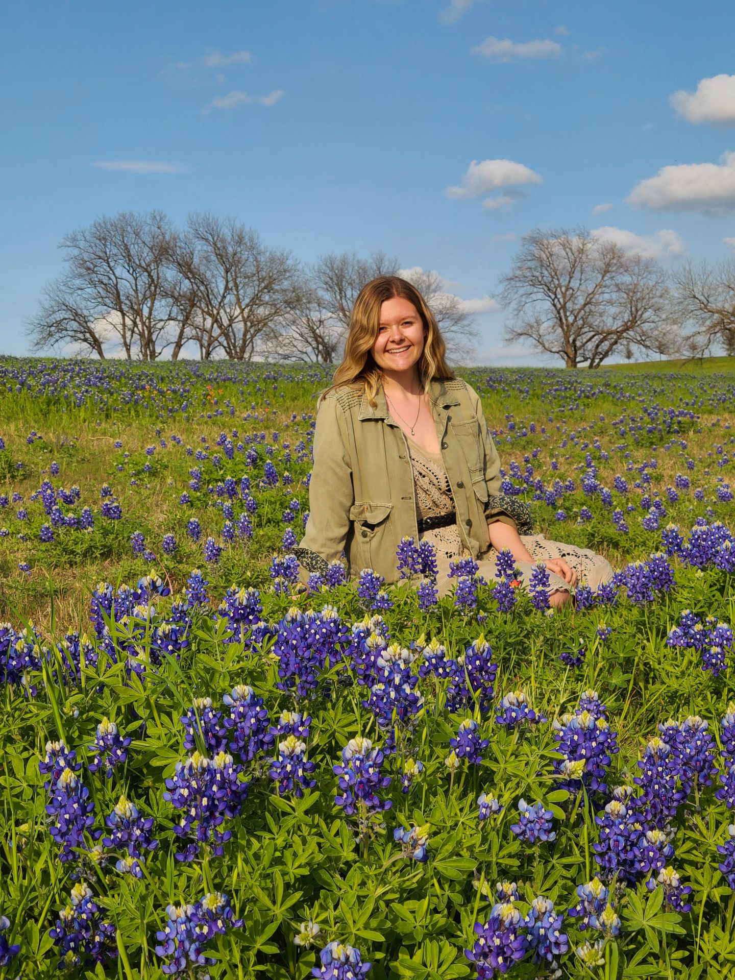 Lydia sitting behind some bluebonnets in a field.