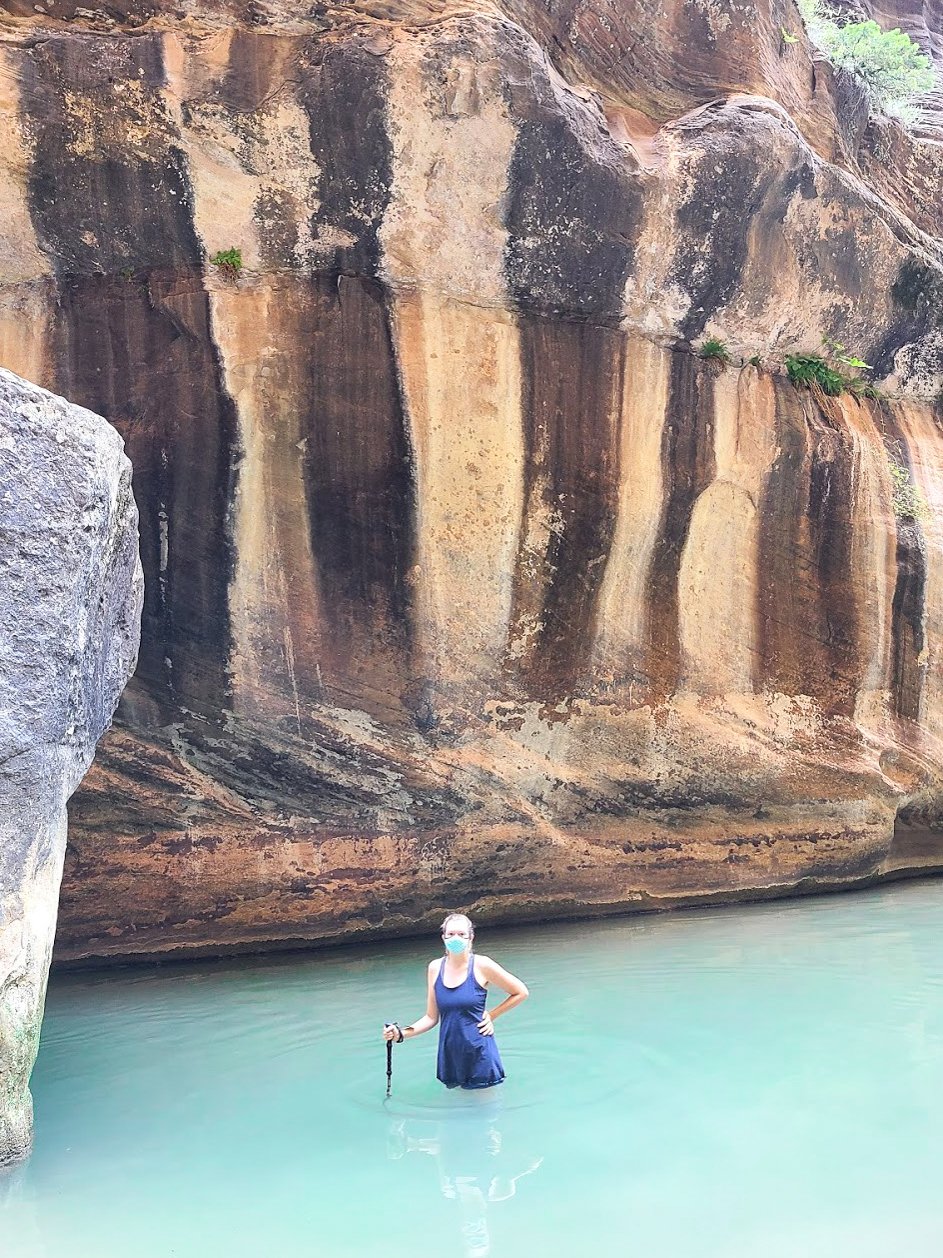 Lydia standing waist deep in the water on The Narrows trail in Zion National Park.