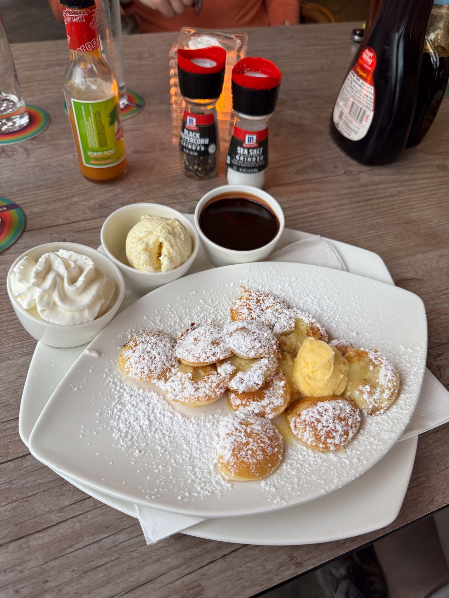Mini pancakes covered in powdered sugar, served with chocolate, butter and whipped cream
