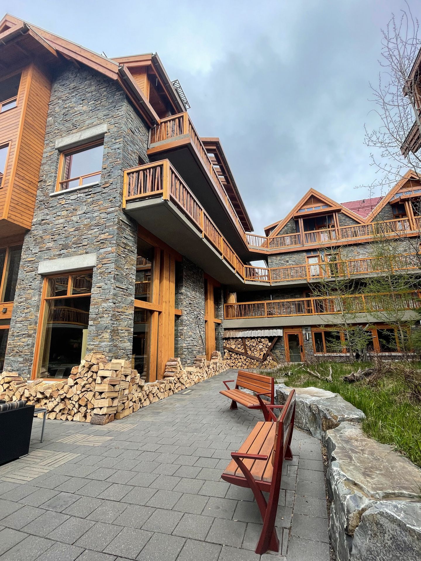 A building with gray stones and balconies made of brown wood. There are some benches on the path outside.