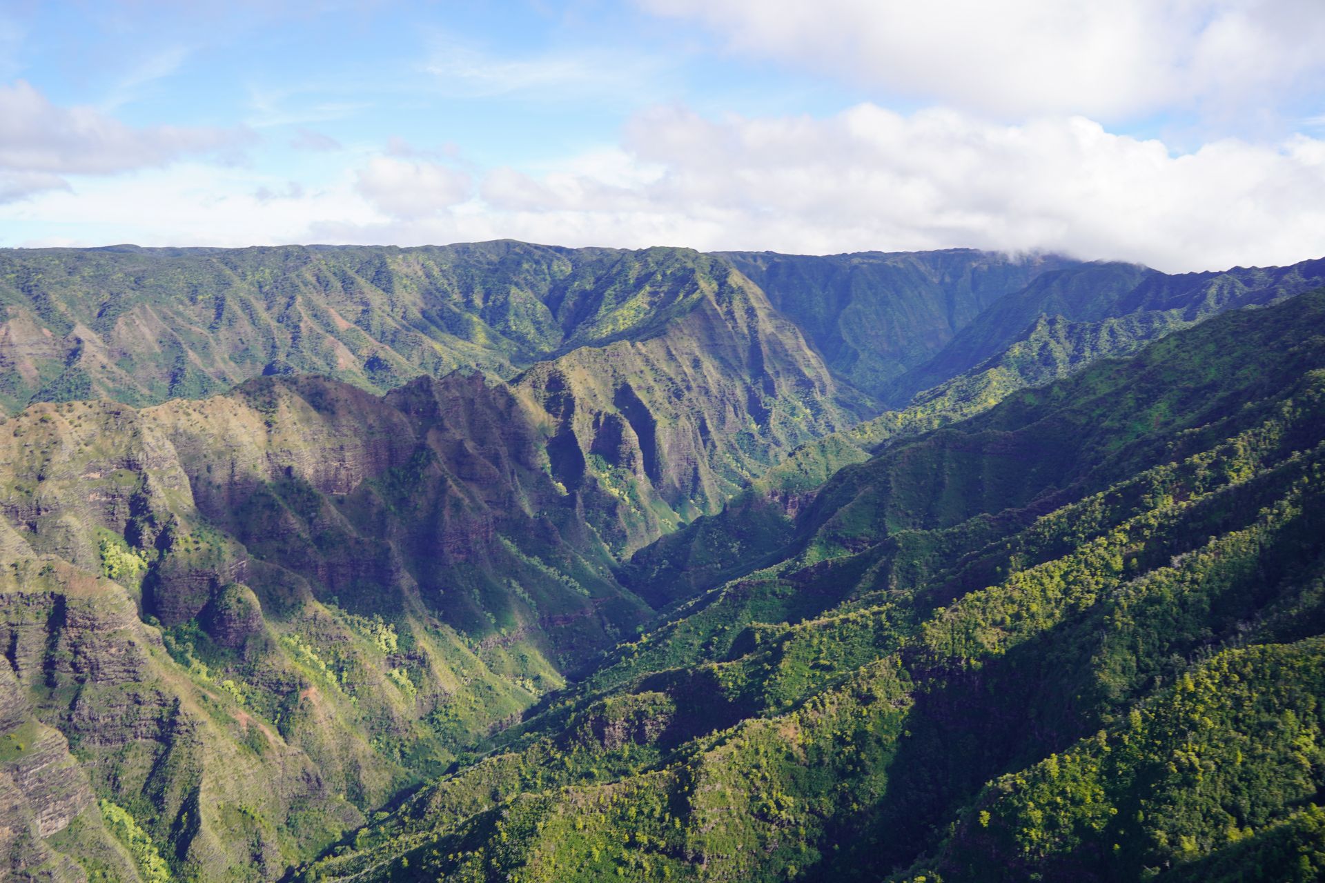 A view of jagged mountains covered in greenery, seen from a doors-off helicopter tour in Kauai