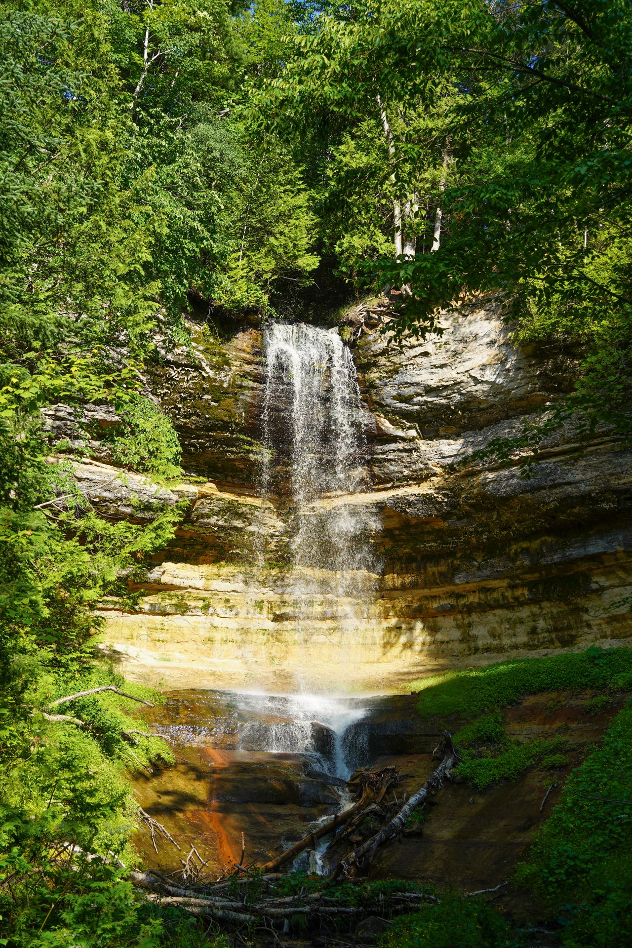 Looking up a waterfall surrounded by green trees.