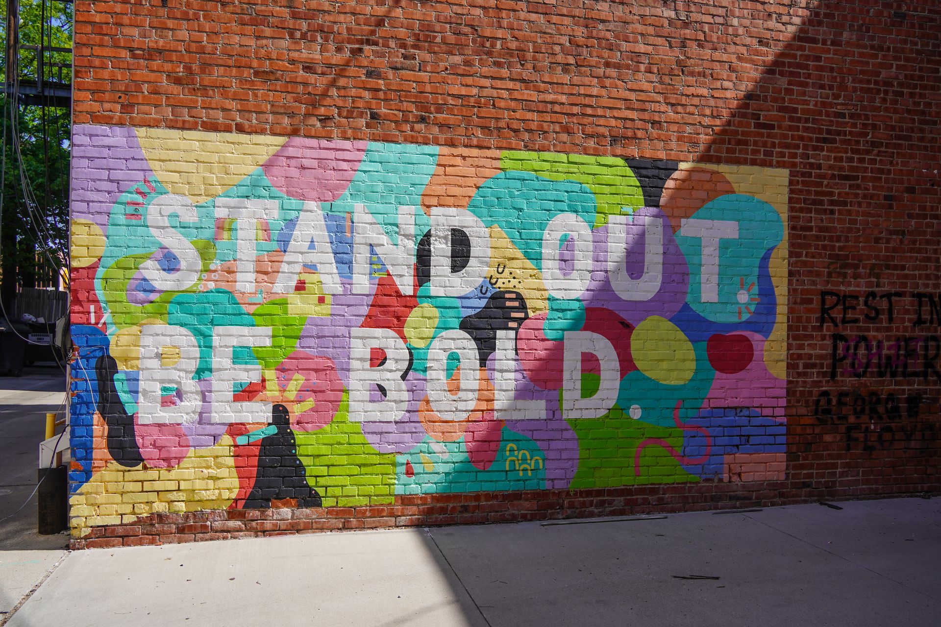 A colorful mural that reads 'Stand Out. Be Bold' in an Art Alleyway in Downtown Kearney