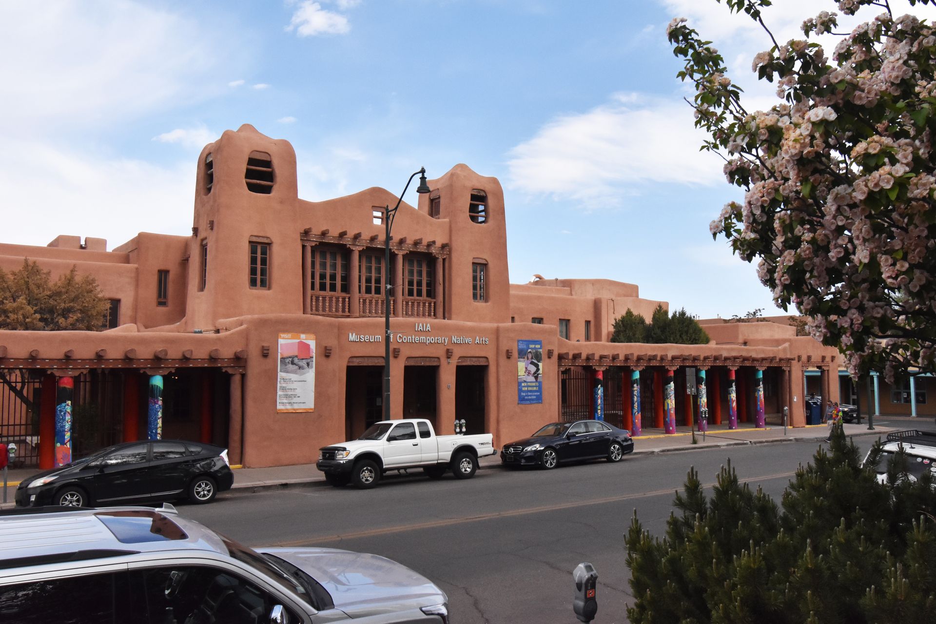 The exterior of the Museum of Contemporary Native Arts. There are overhangs with colorful columns on the sidewalks leading to the entrance.