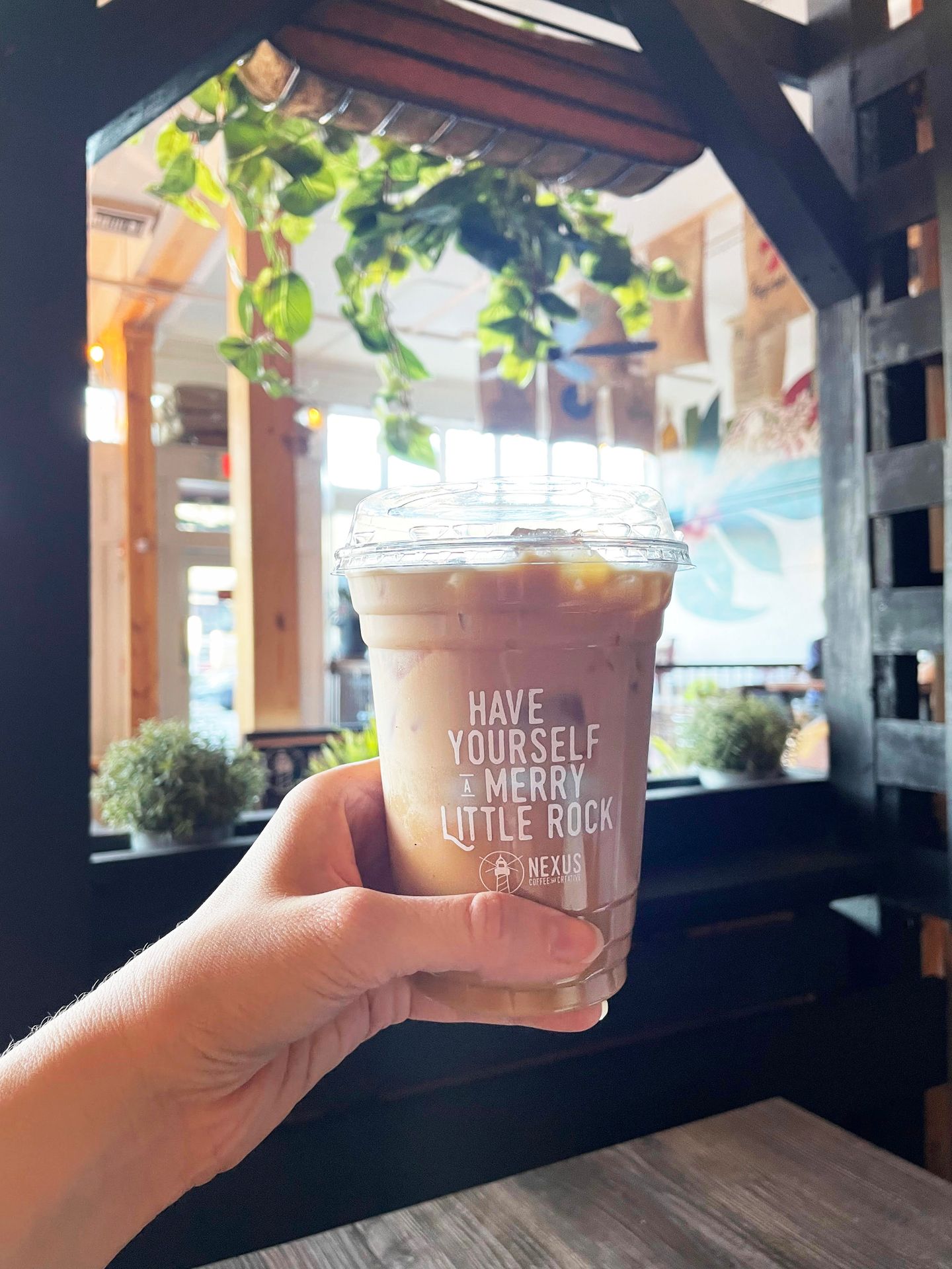 Holding up an iced latte with a cup labeled "Have yourself a Merry Little Rock" inside of Fidel & Co