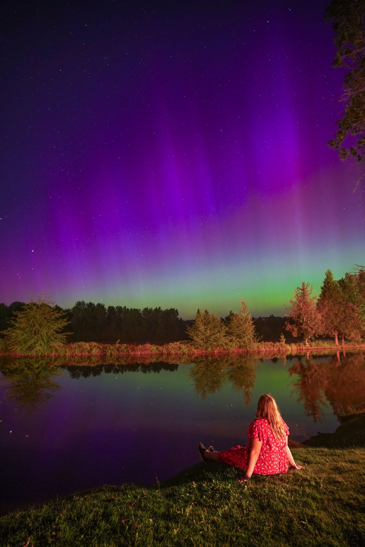 Lydia sitting on the shore and looking up at the Norhtern Lights at Bridgeview Winery
