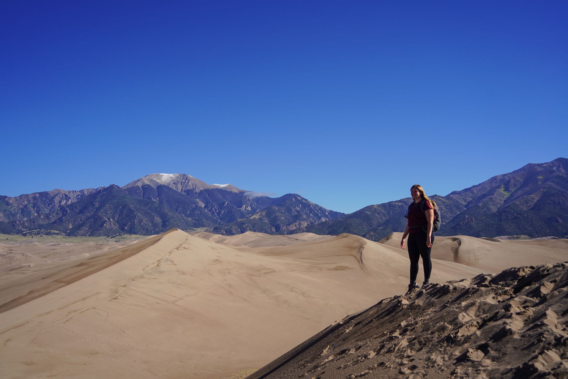 Lydia on a steep sand dune, with more sand dunes in the distance