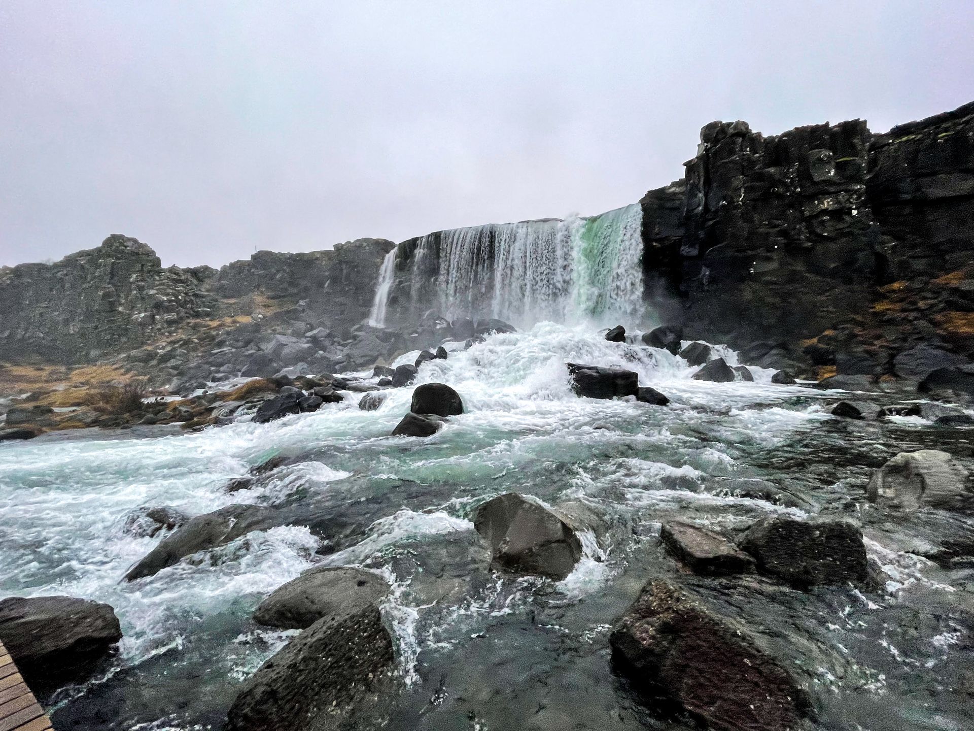 A wide waterfall cascading down a cliff of black rocks.