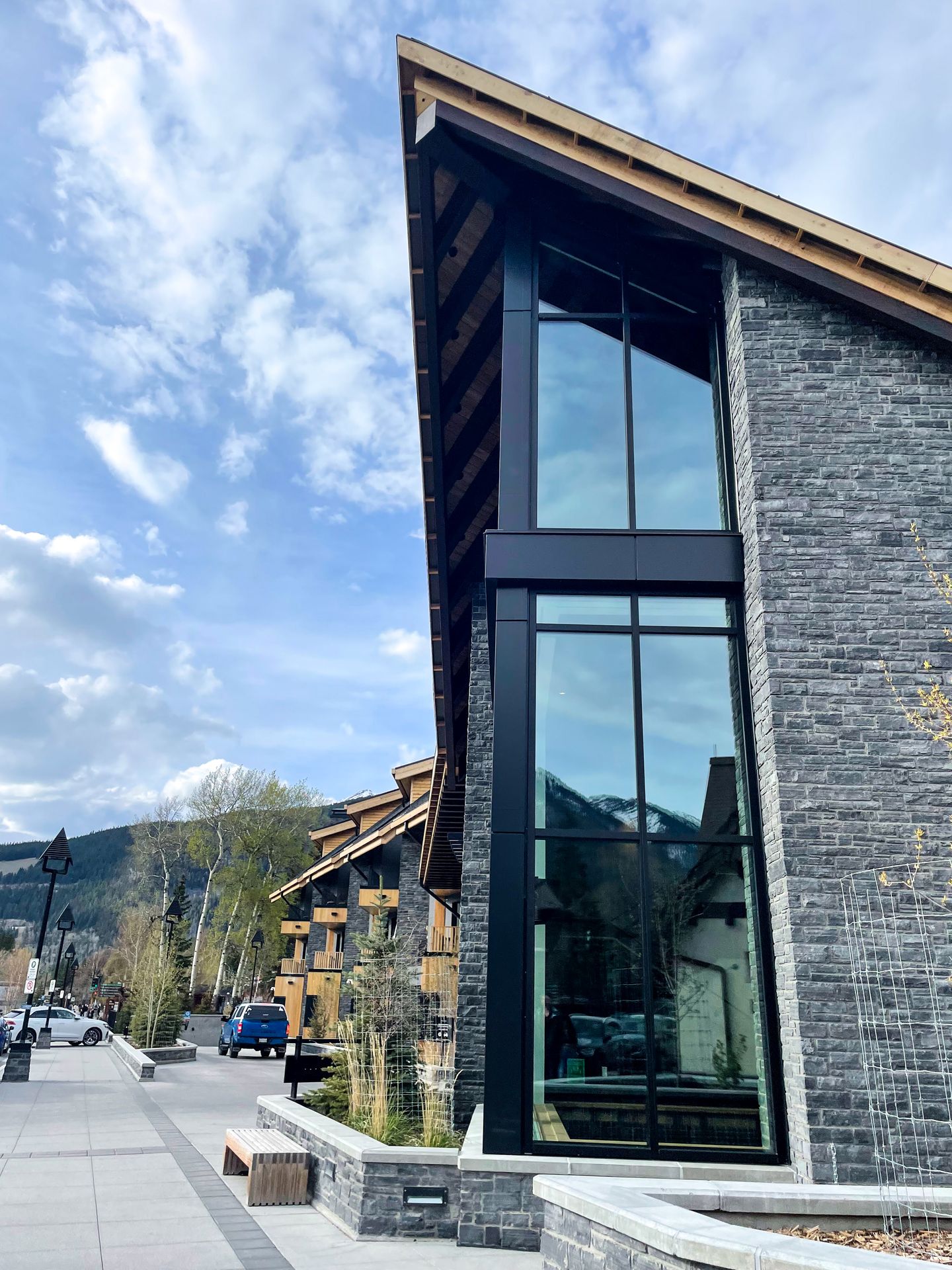 A gray, brick building with floor to ceiling windows. The shape of the building is inspired by a mountain peak.
