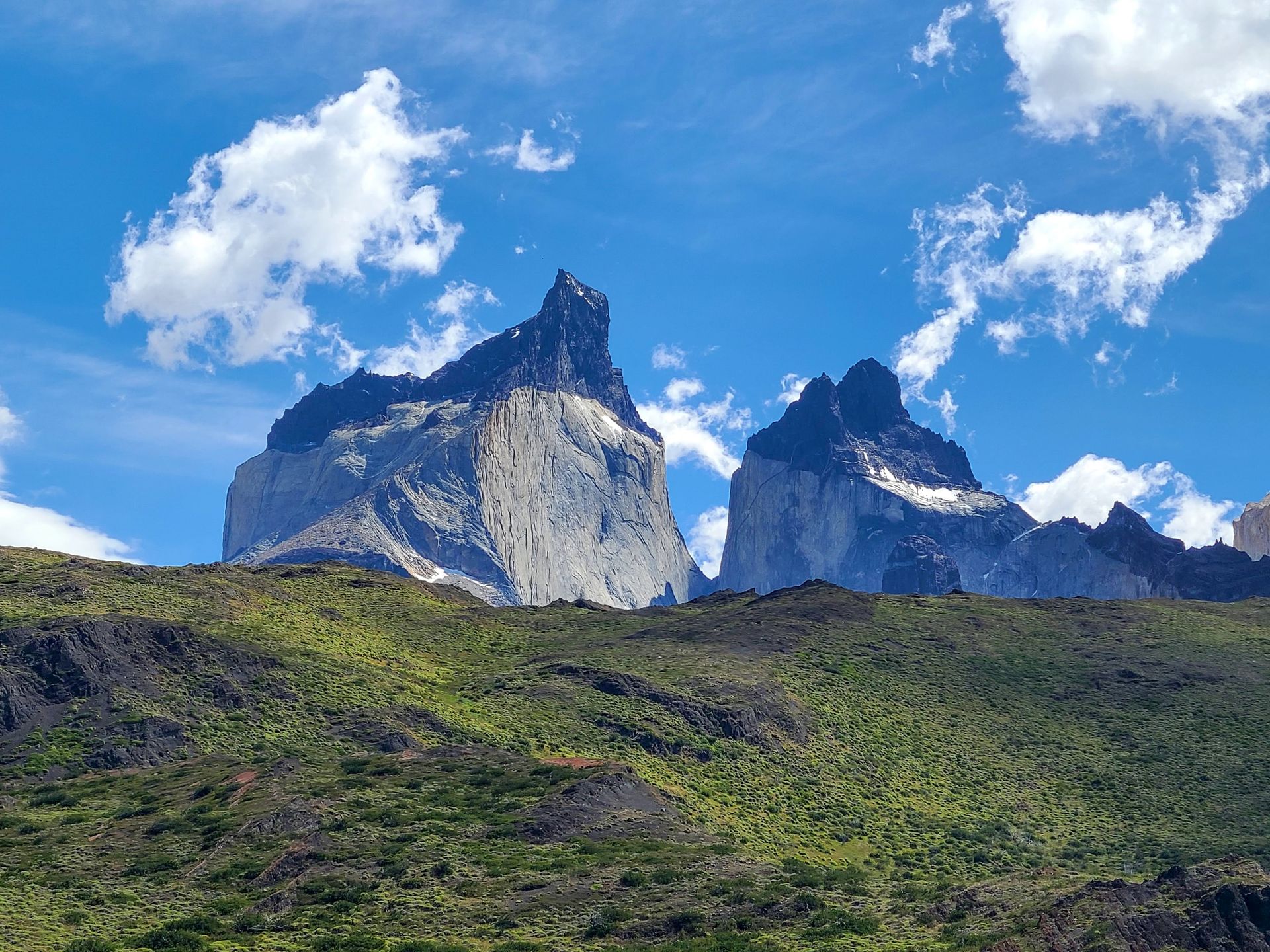 Jagged mountain peaks in the background and a green hill in the foreground.
