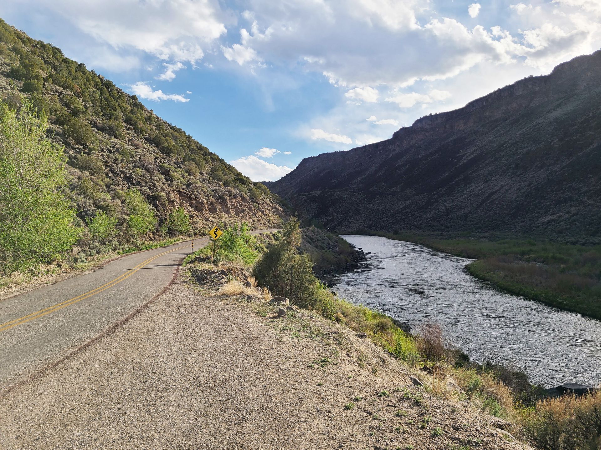 A road next to a river with a canyon walls on both sides.