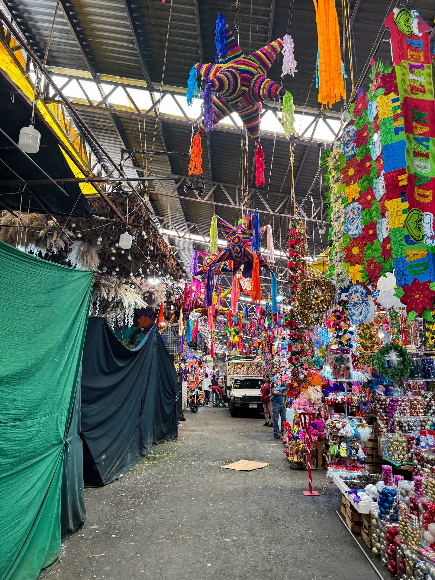 A market with colorful pinatas hanging from the ceiling and lining the pathway.