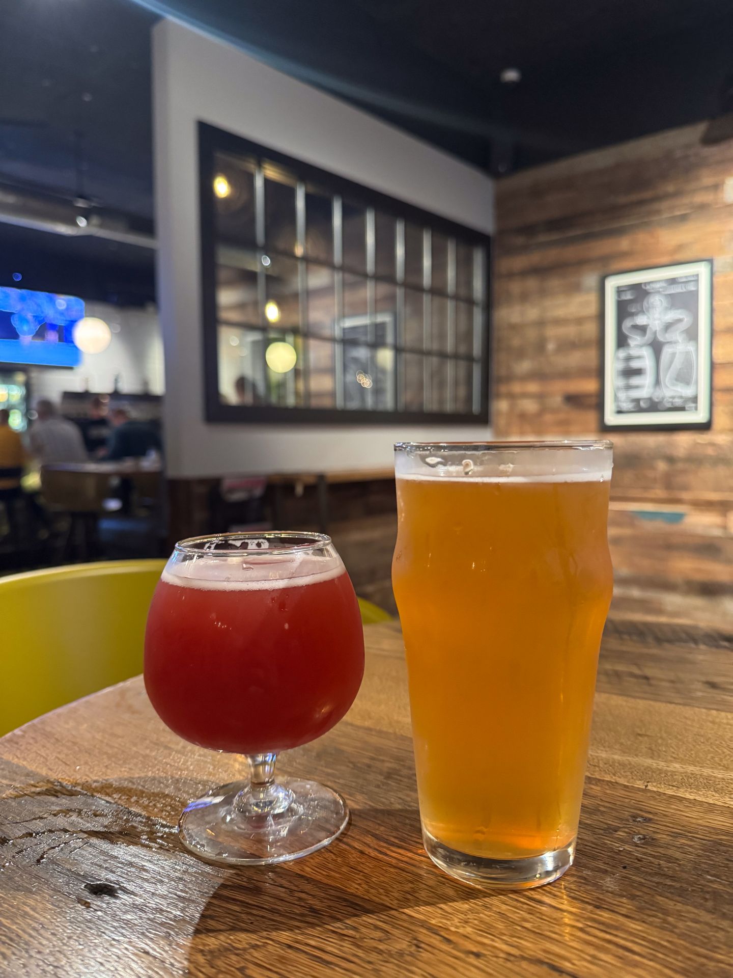 Two beers from Pies and Pints, one is in a short glass and red, the other is tall and a yellow color