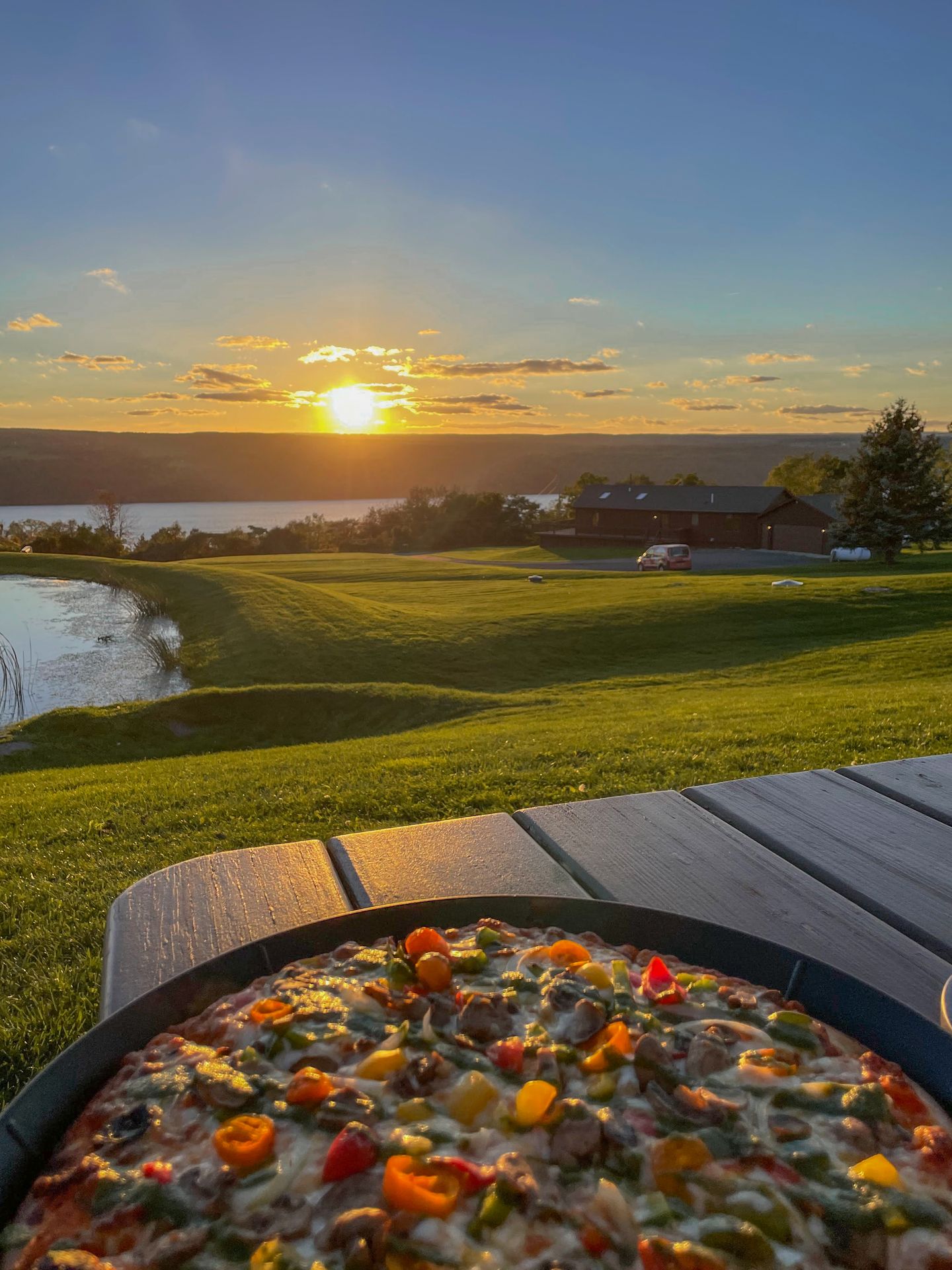 Looking at a pizza sitting outside on a picnic table, with the sun setting in the sky.