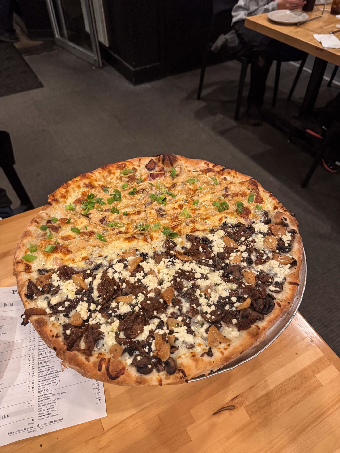 A pizza that has different flavors on each half. One side has mushrooms, while the other has chicken and green onions