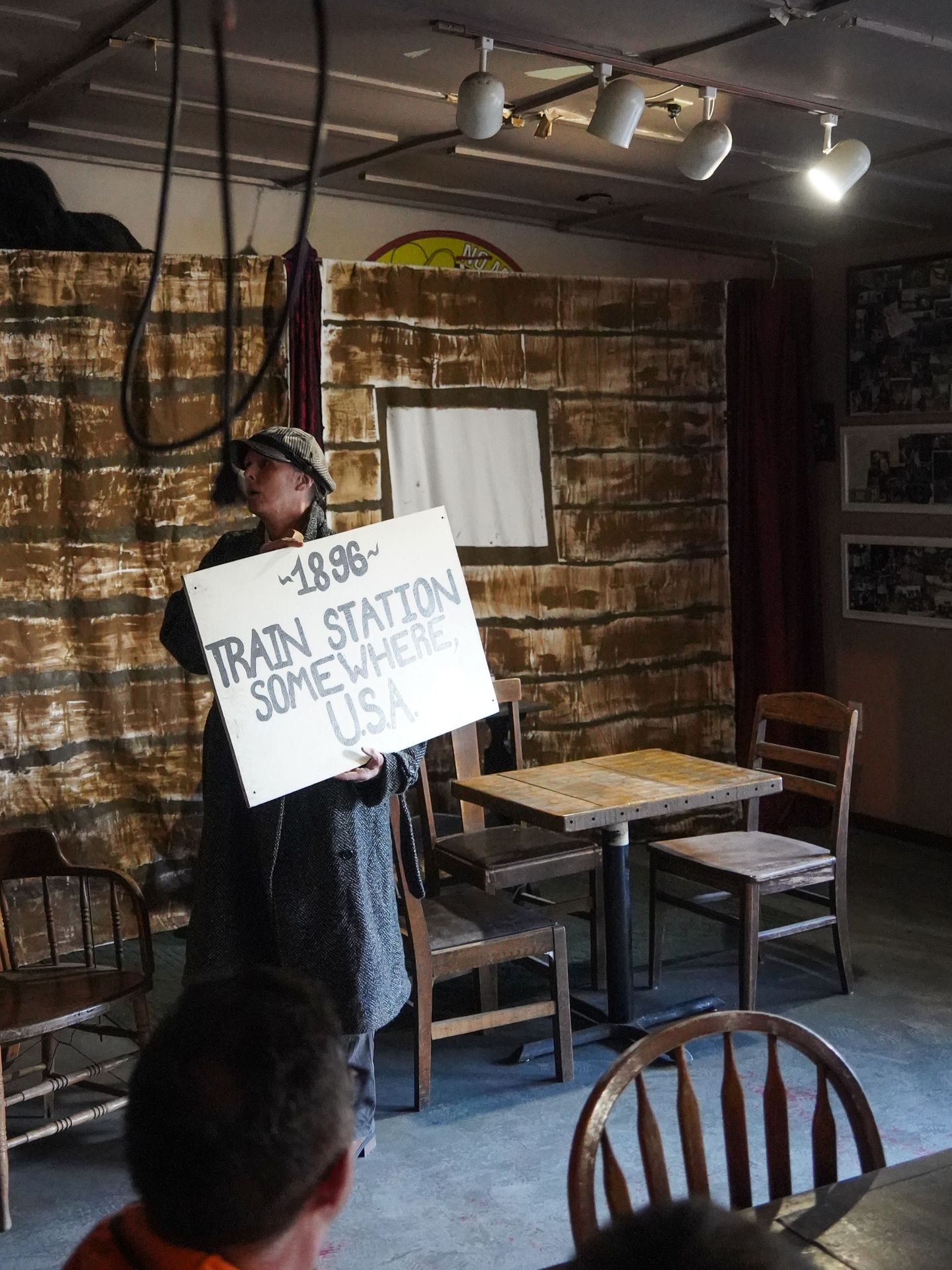 An actor walking with a sign that read '1896 - Train station somewhere USA' during the McCarthy Rose play