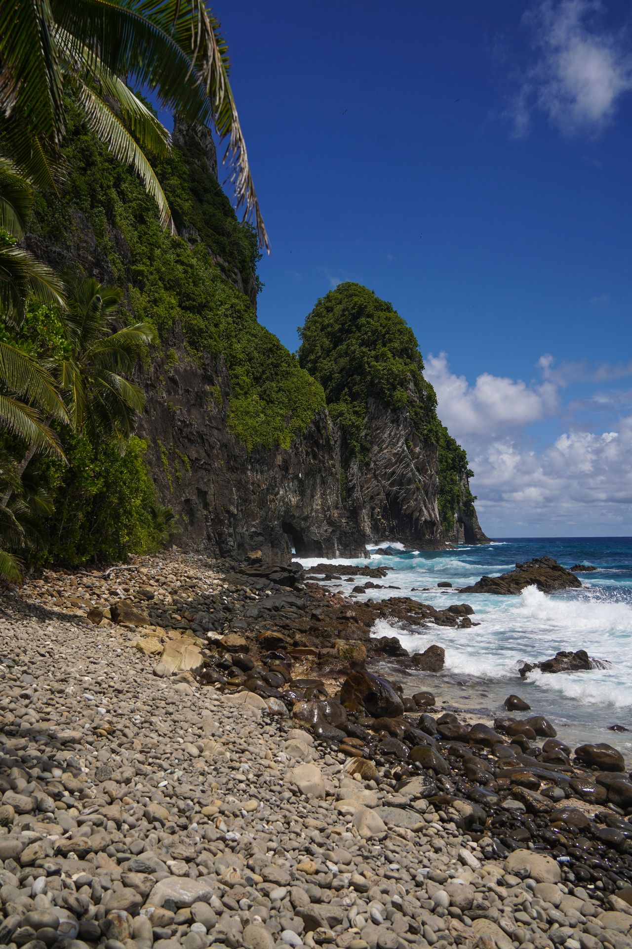 A rocky beach with a small, tall island in the distance