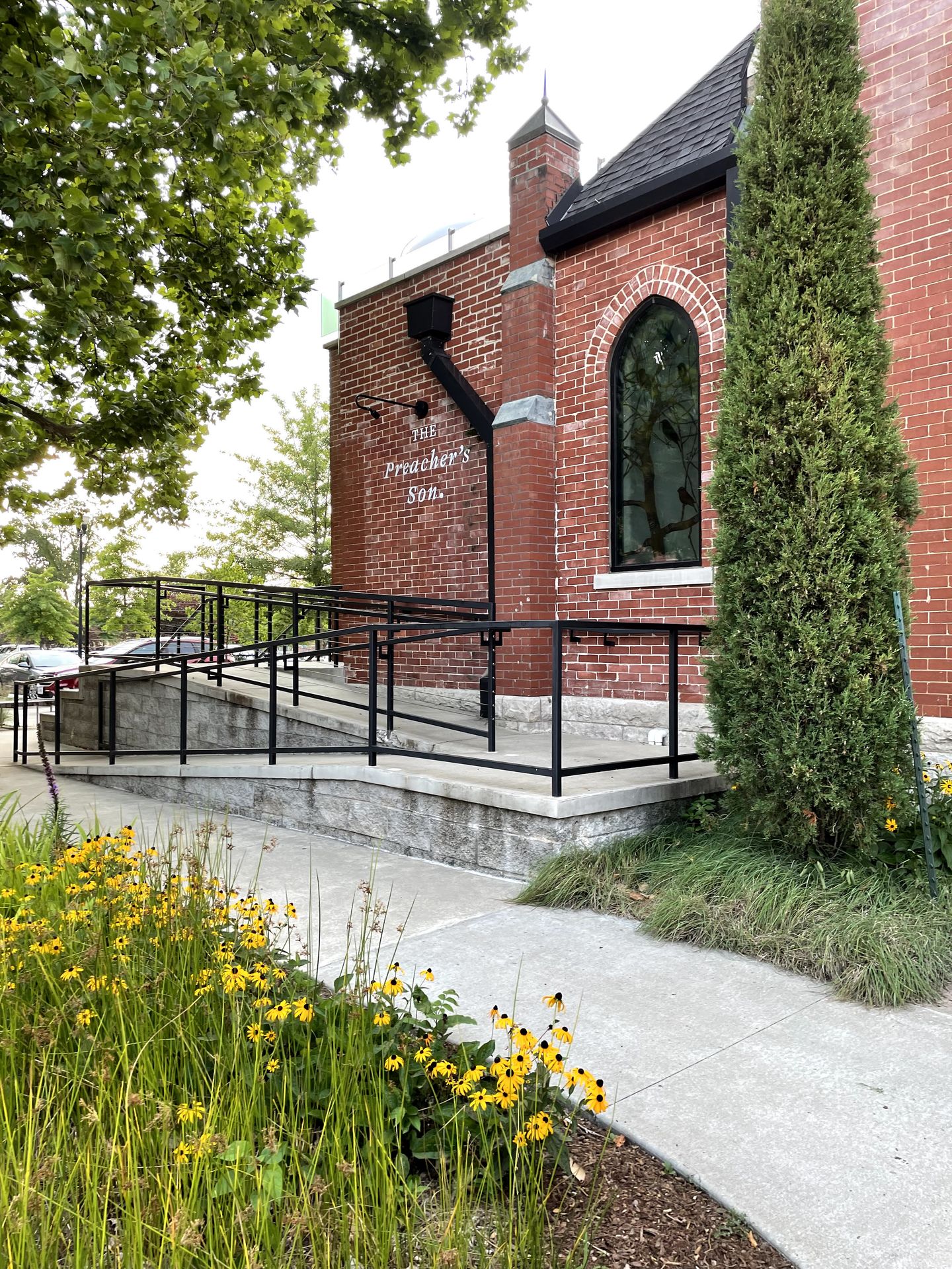 The brick exterior of The Preacher's Son. There are yellow flowers in front of the building