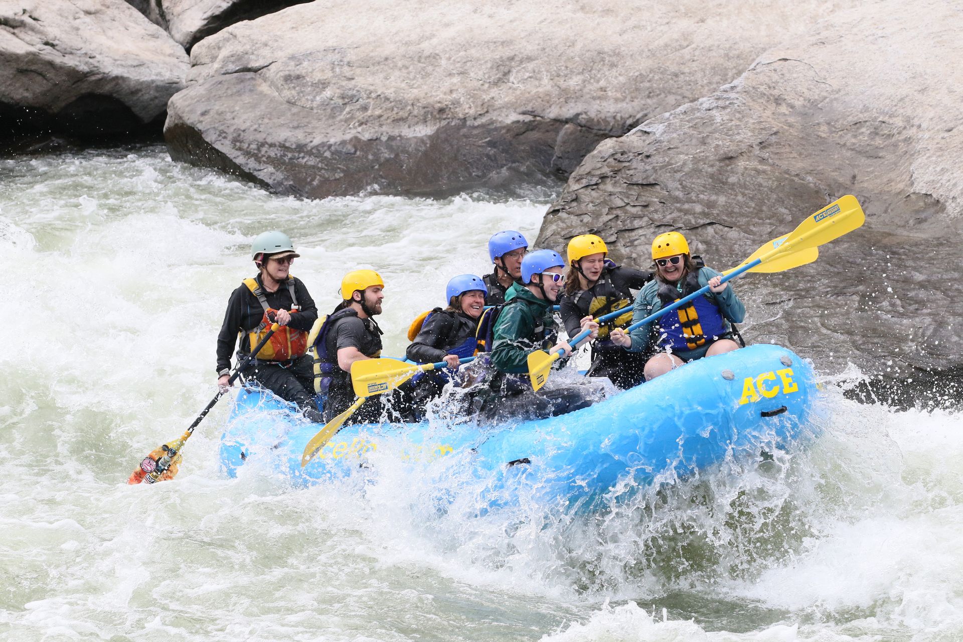 Lydia and a group of others going over a rapid next to a huge boulder, while rafting on the New River