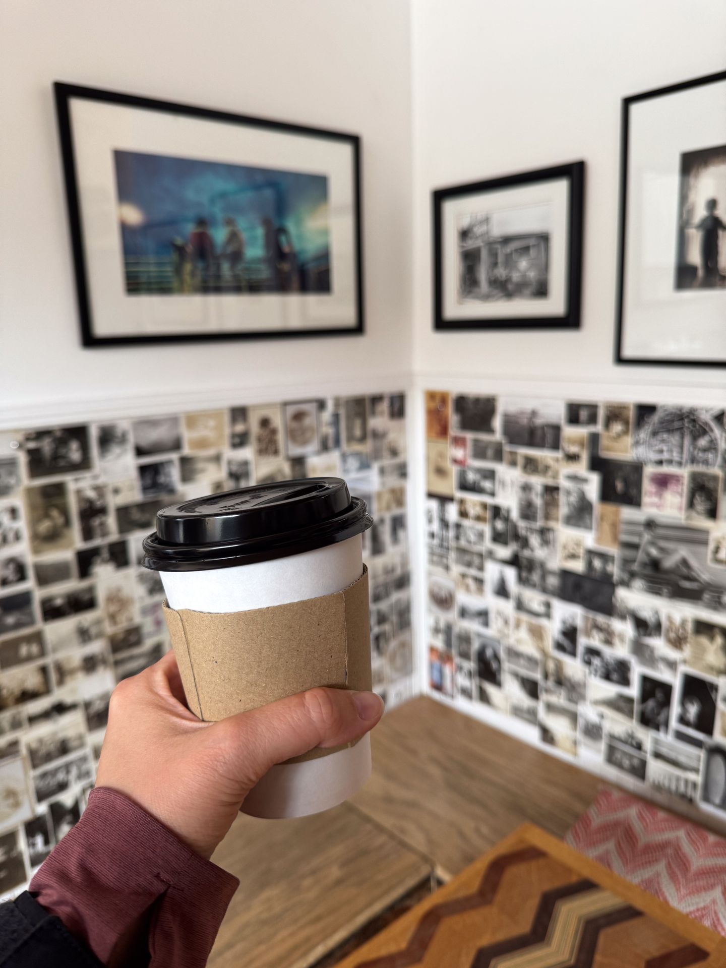 Holding up a coffee inside of Range Finder. There is a wall in the background covered with photos.