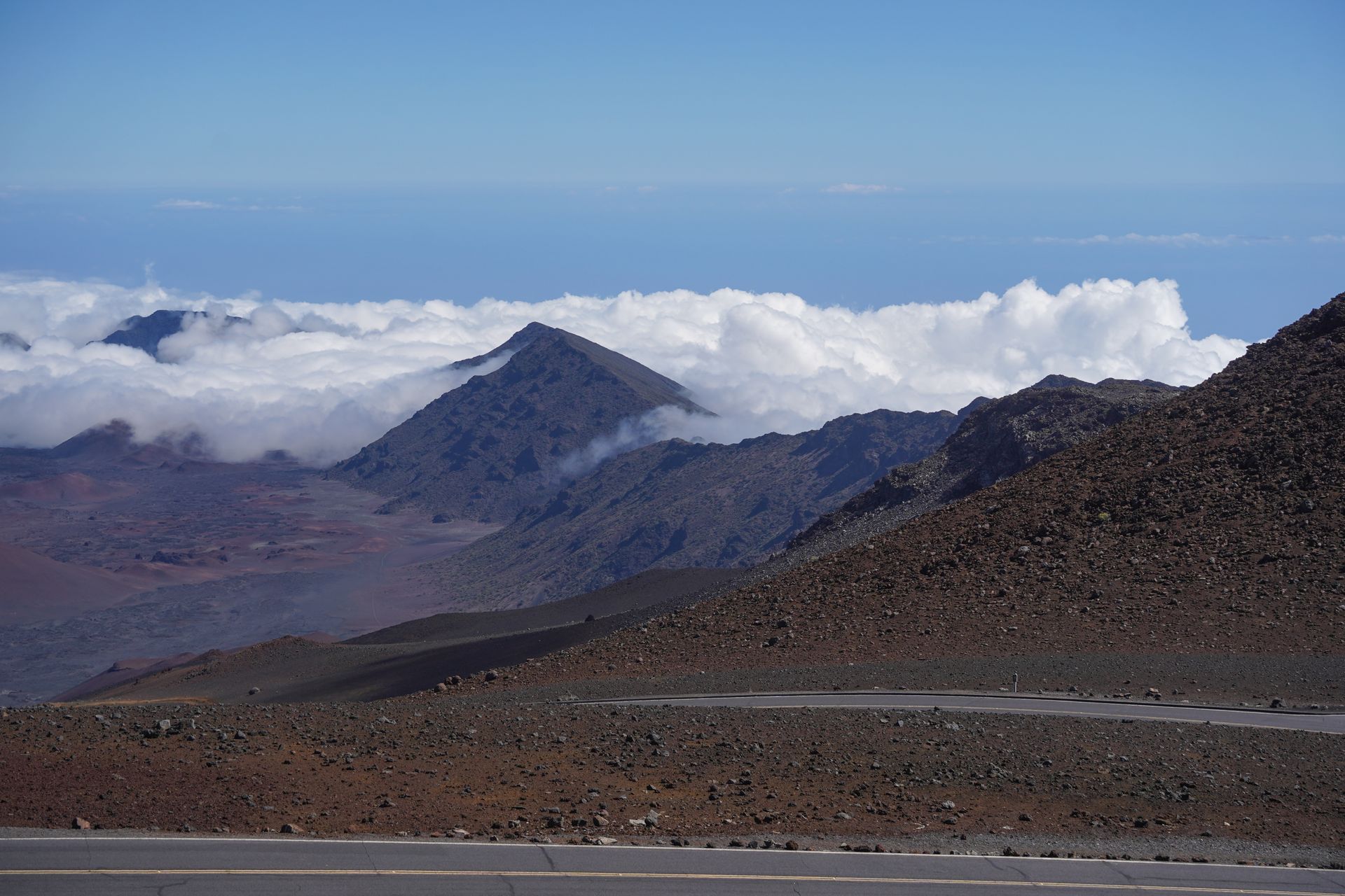 Looking at a road, that winds next to mountains. Some peaks are partially obscured by clouds