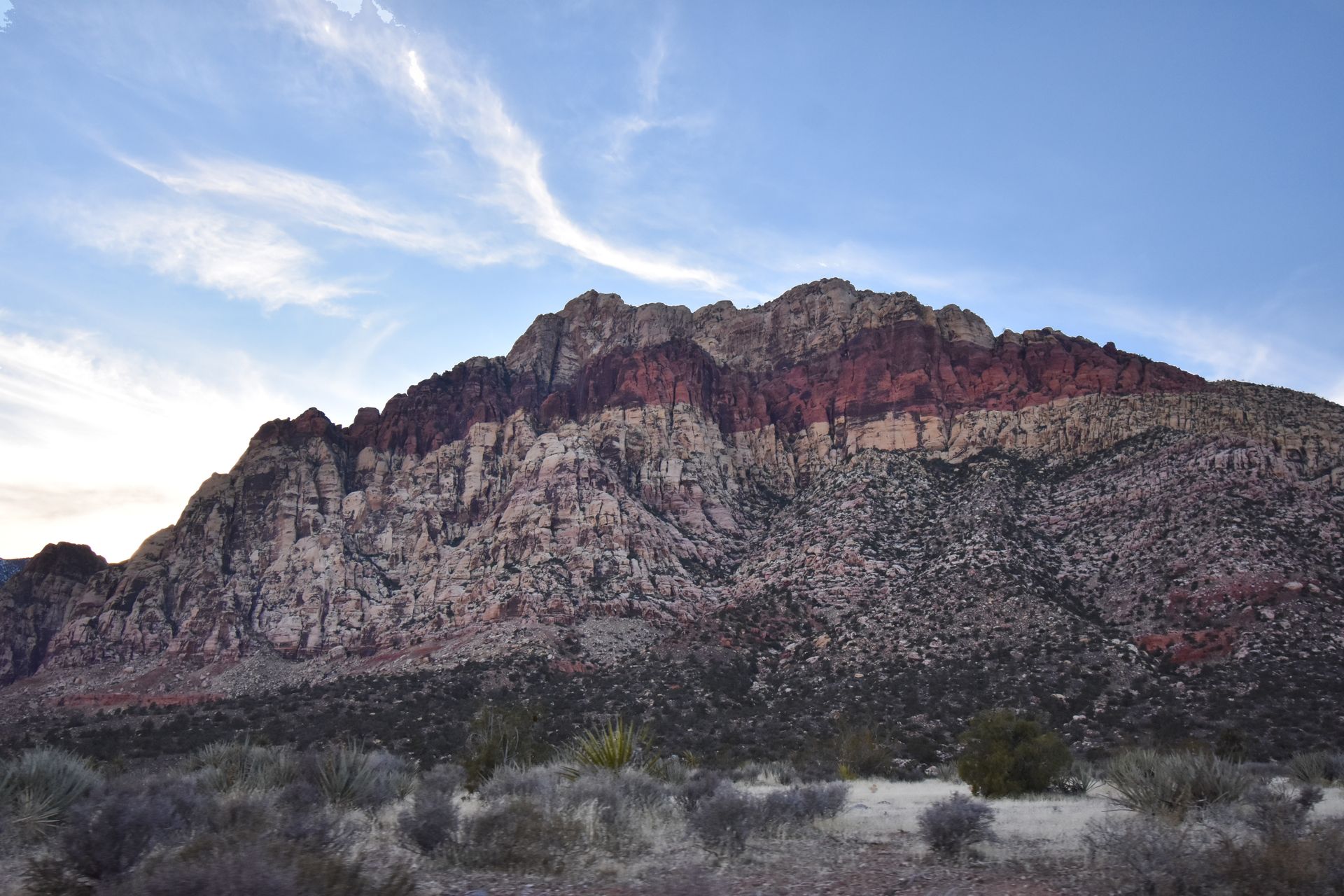 A canyon wall striped with varying colors of red rocks.