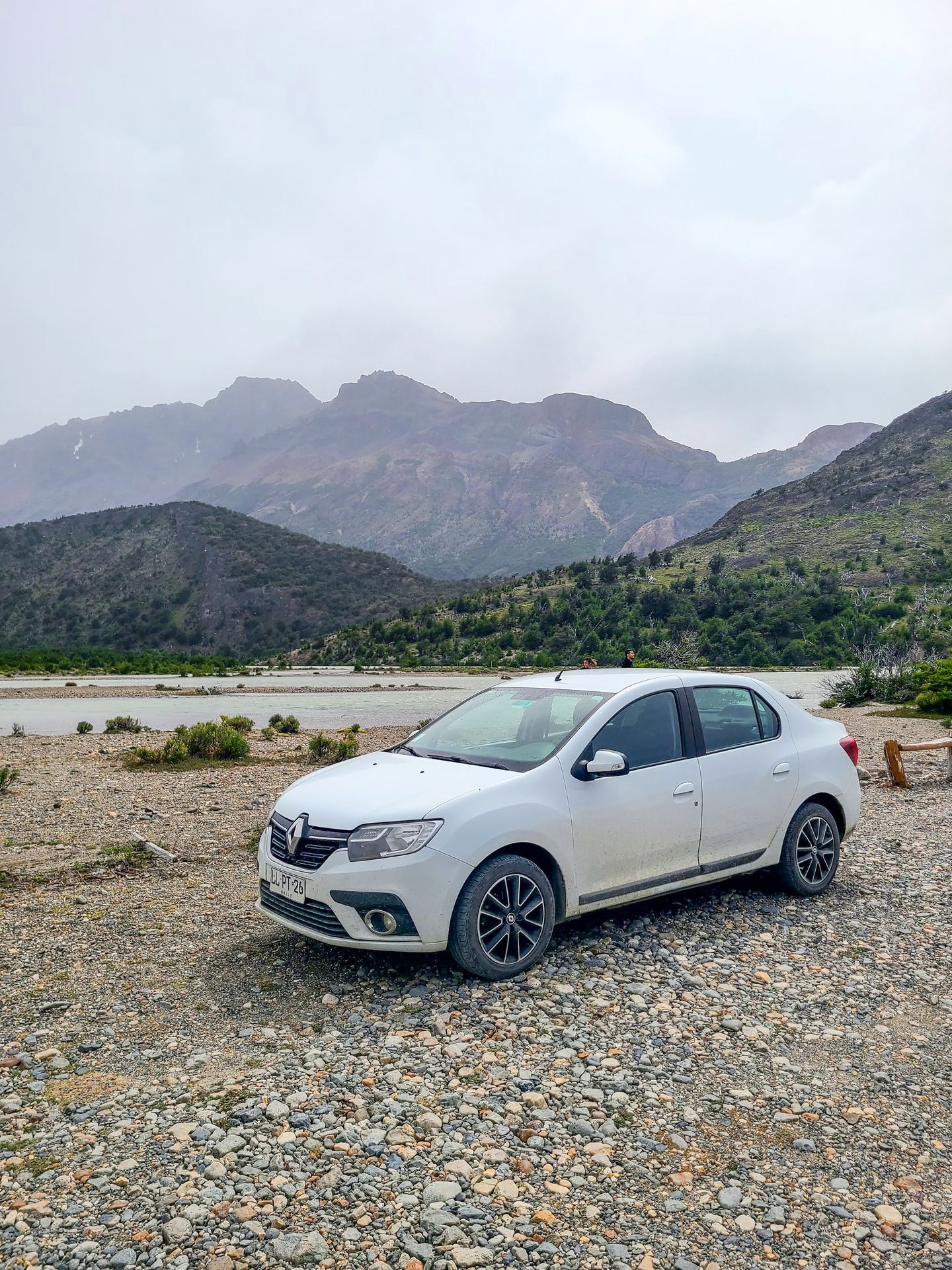 A small, white car on a rocky road with mountains in the background.