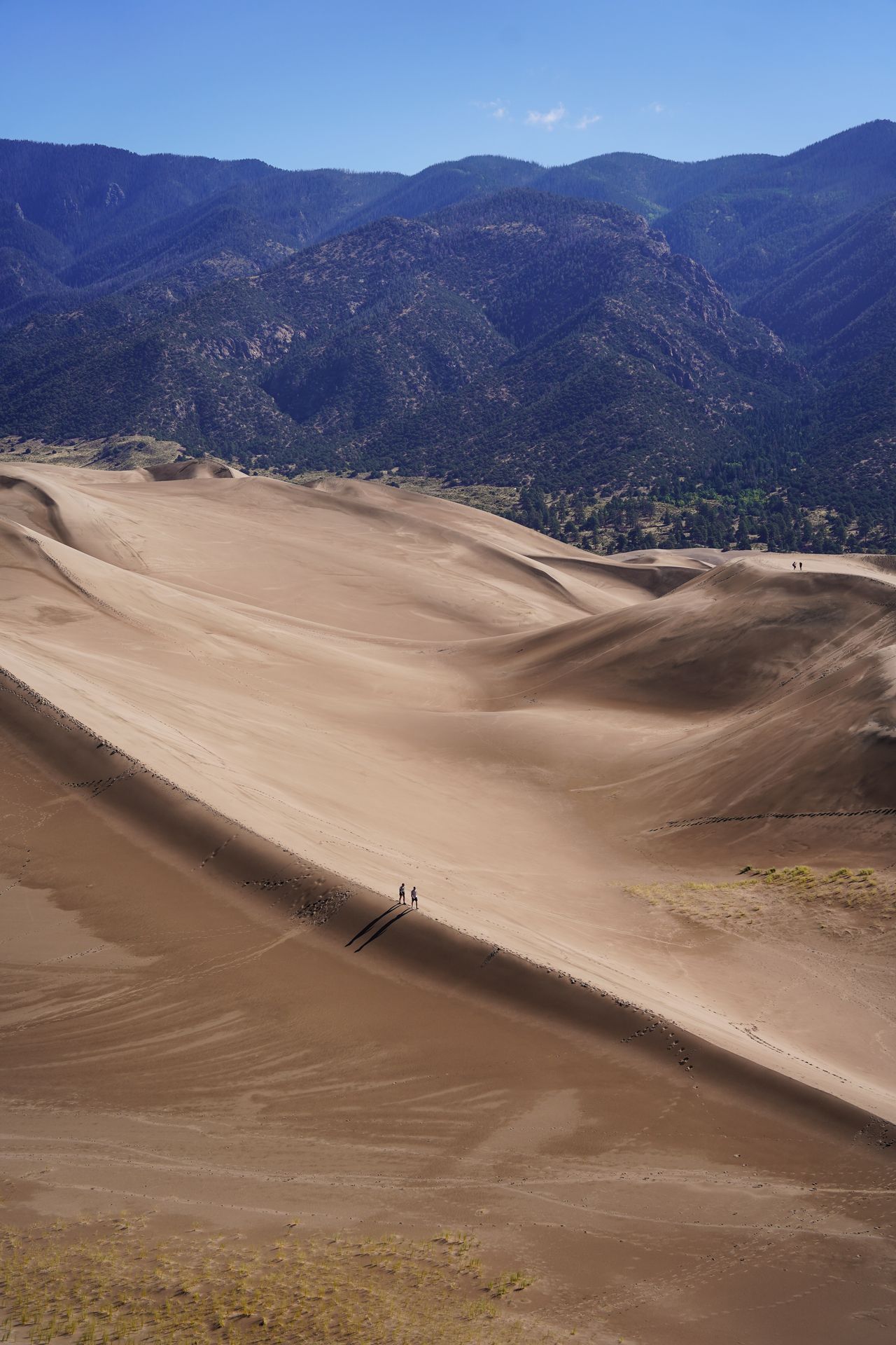 A couple hiking on top of a steep ridge of sand in Great Sand Dunes