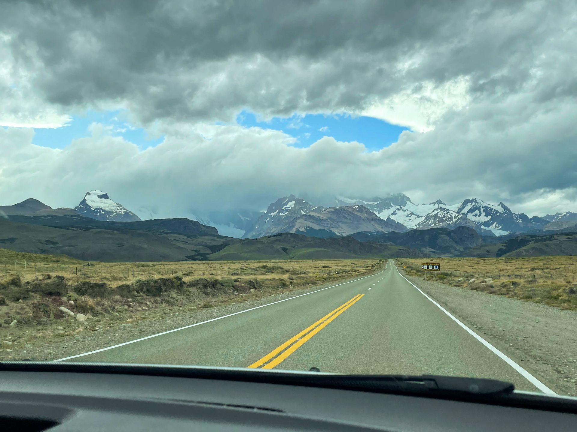 A long road that leads up an area of mountains partially covered in snow and ice. Clouds partially obscure the peaks of the mountains.