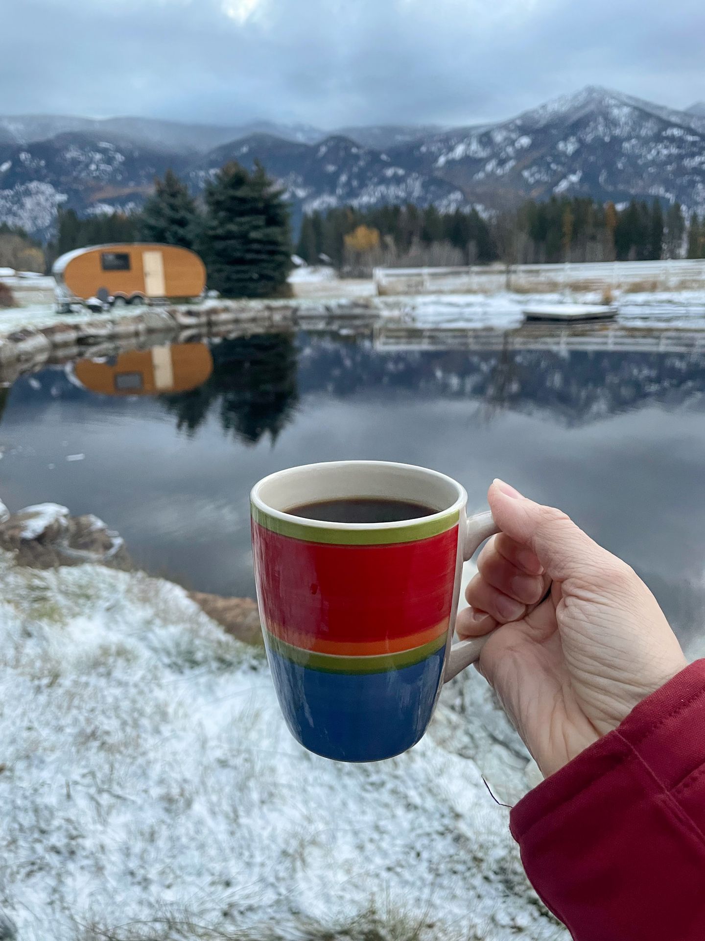 Holding up a striped mug in front of a glamping cabin along the water