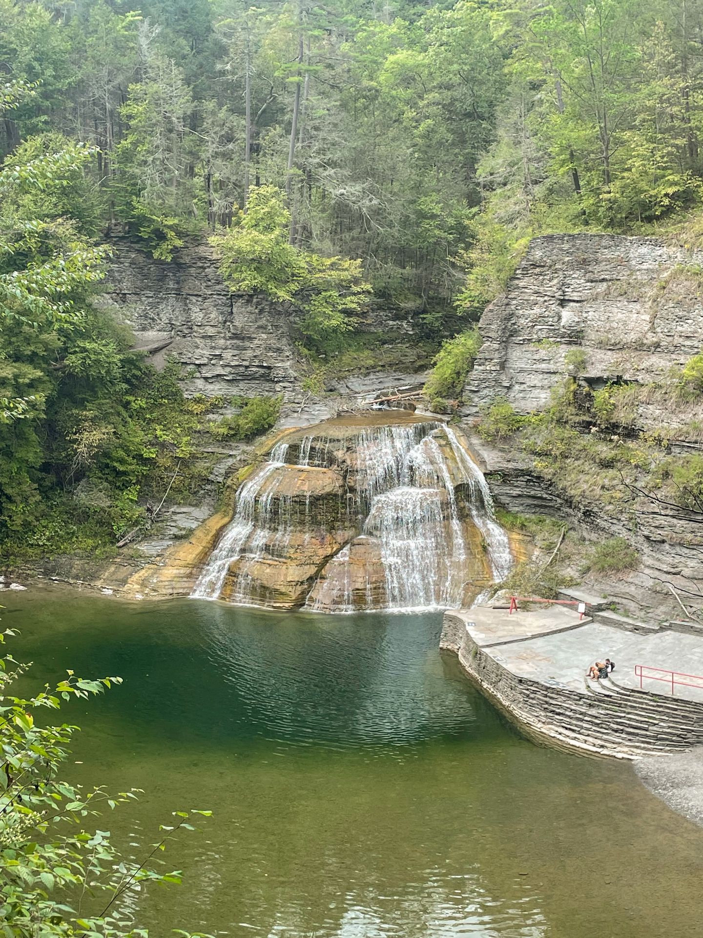 Looking down at a large waterfall at Robert H. Treman. A couple people stand on a flat area at the base of the falls.
