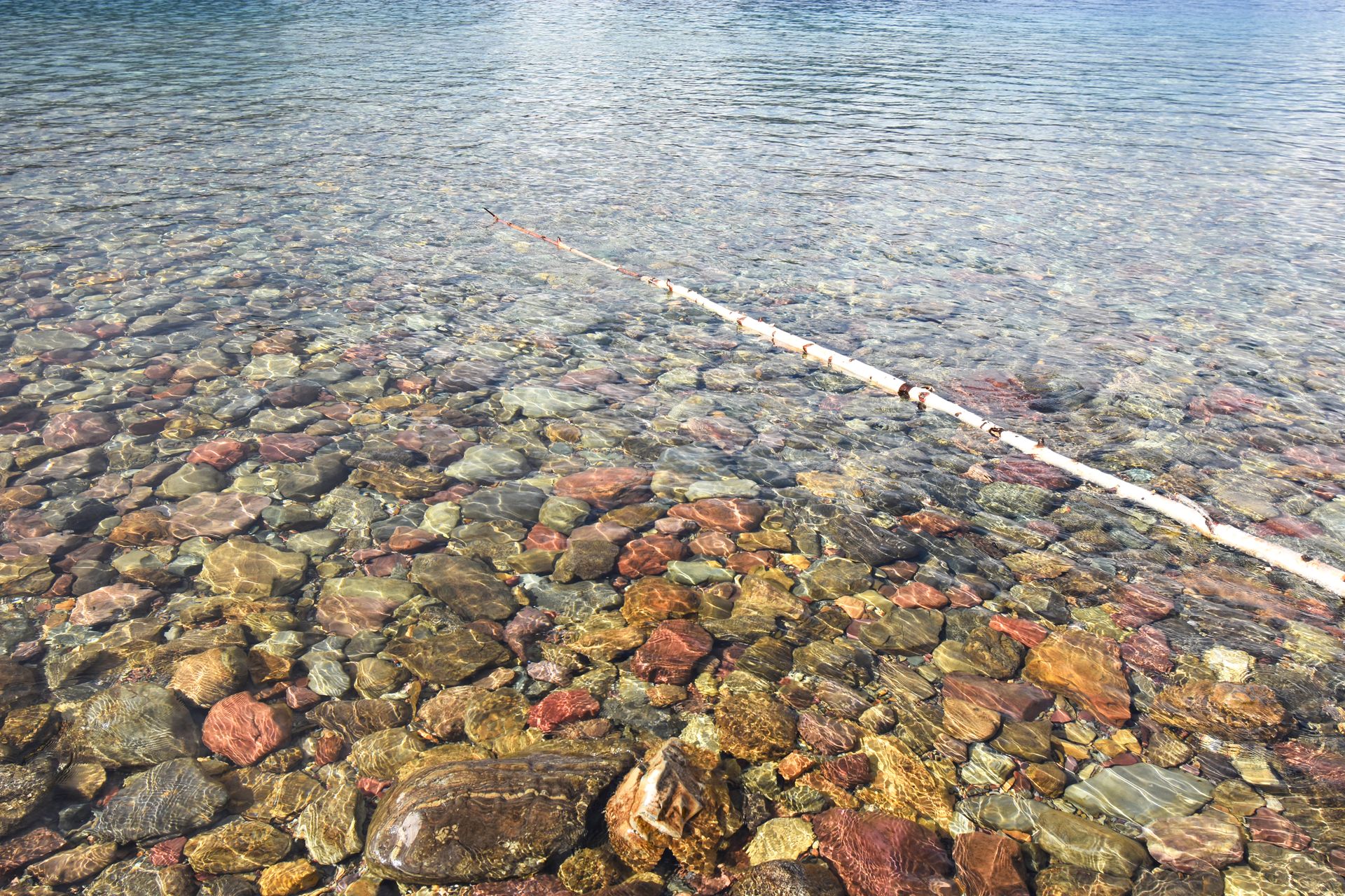 A close up of colorful rocks below the water of Lake McDonald. The rocks are red, yellow and green.