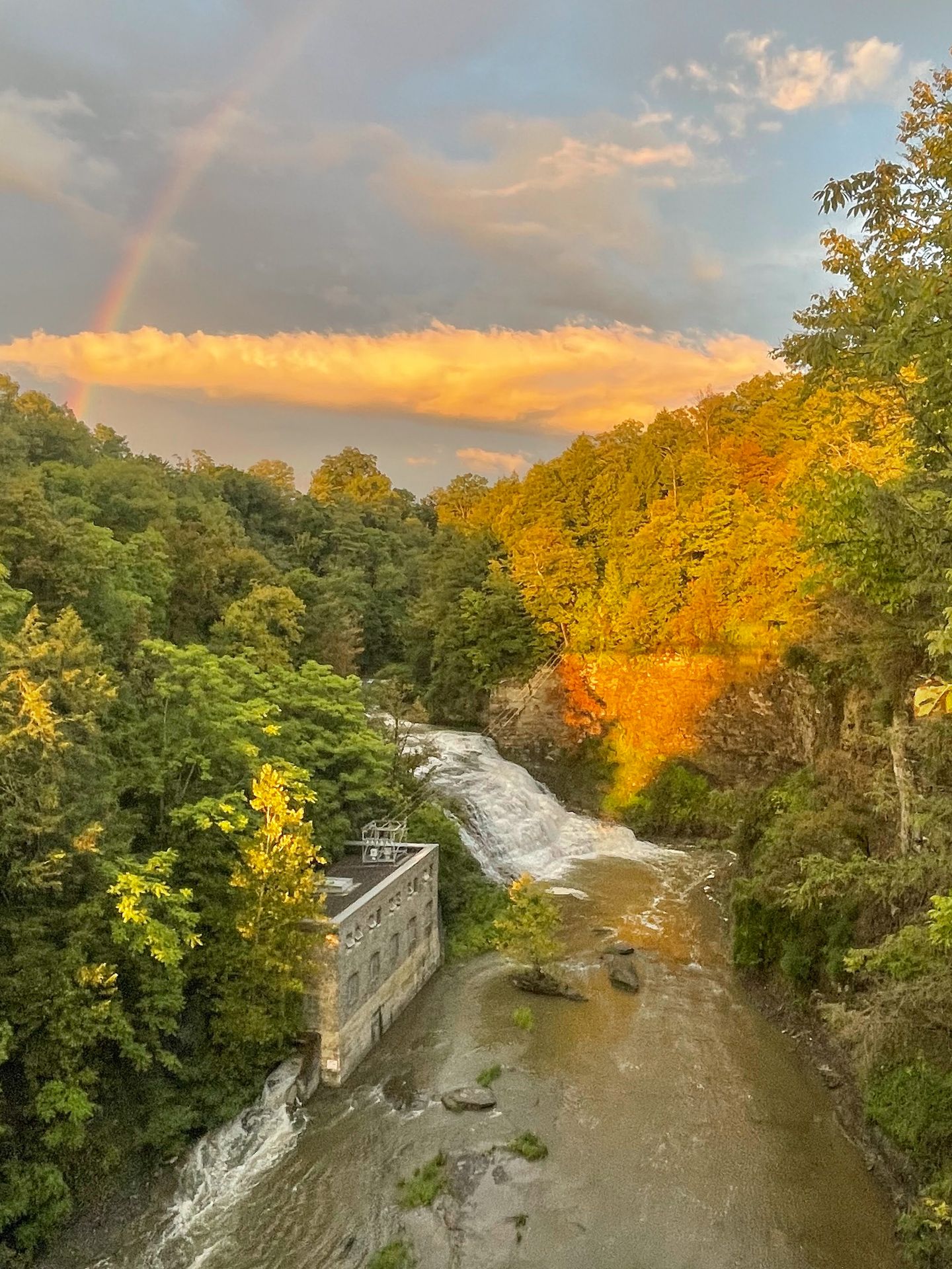 Looking down at a waterfall in a gorge. There is a rainbow in the sky above.