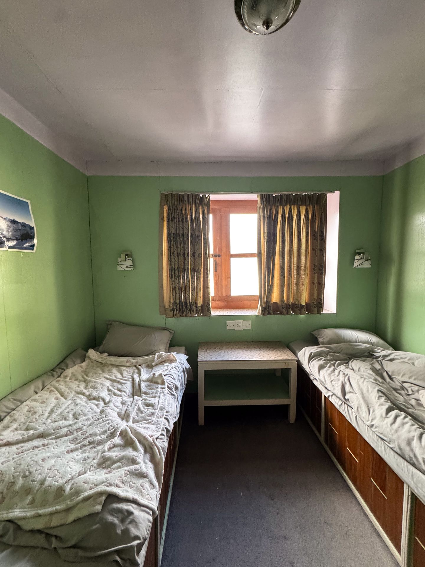 A room with green walls, two twin beds and a window in the center