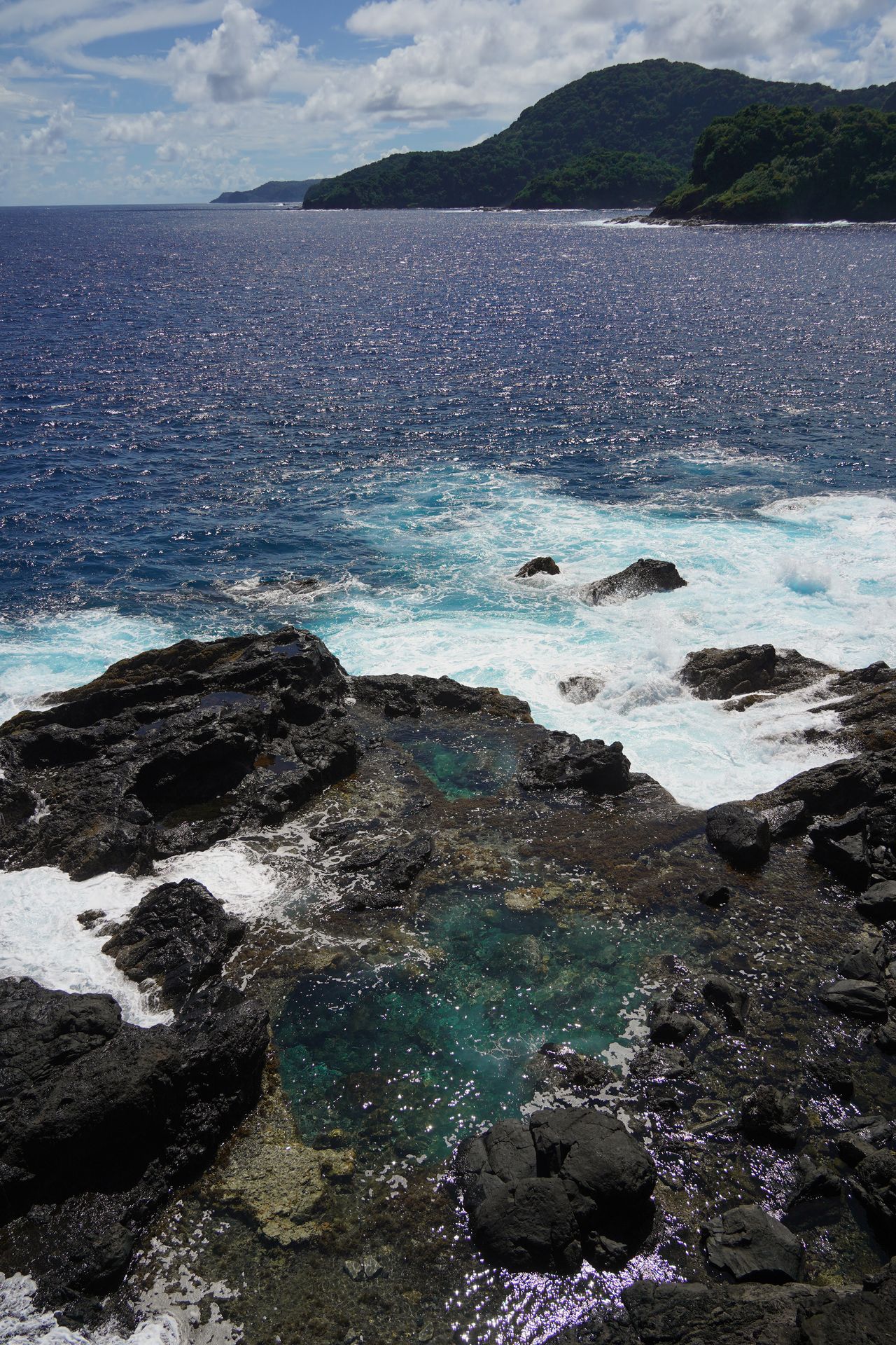 A coastline made up of black, lava rocks with pools of blue water
