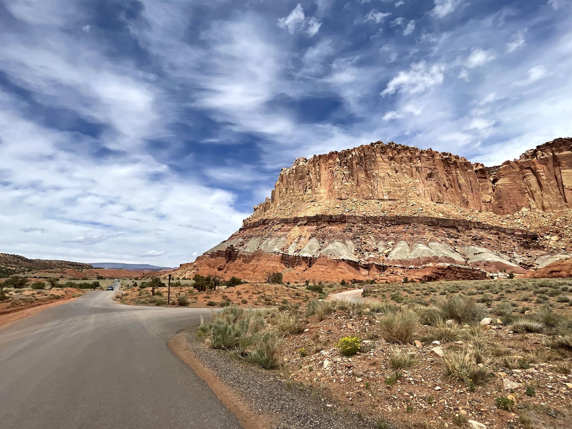 A road with a large cliff next to it. The cliff is striped in various shades of orange.