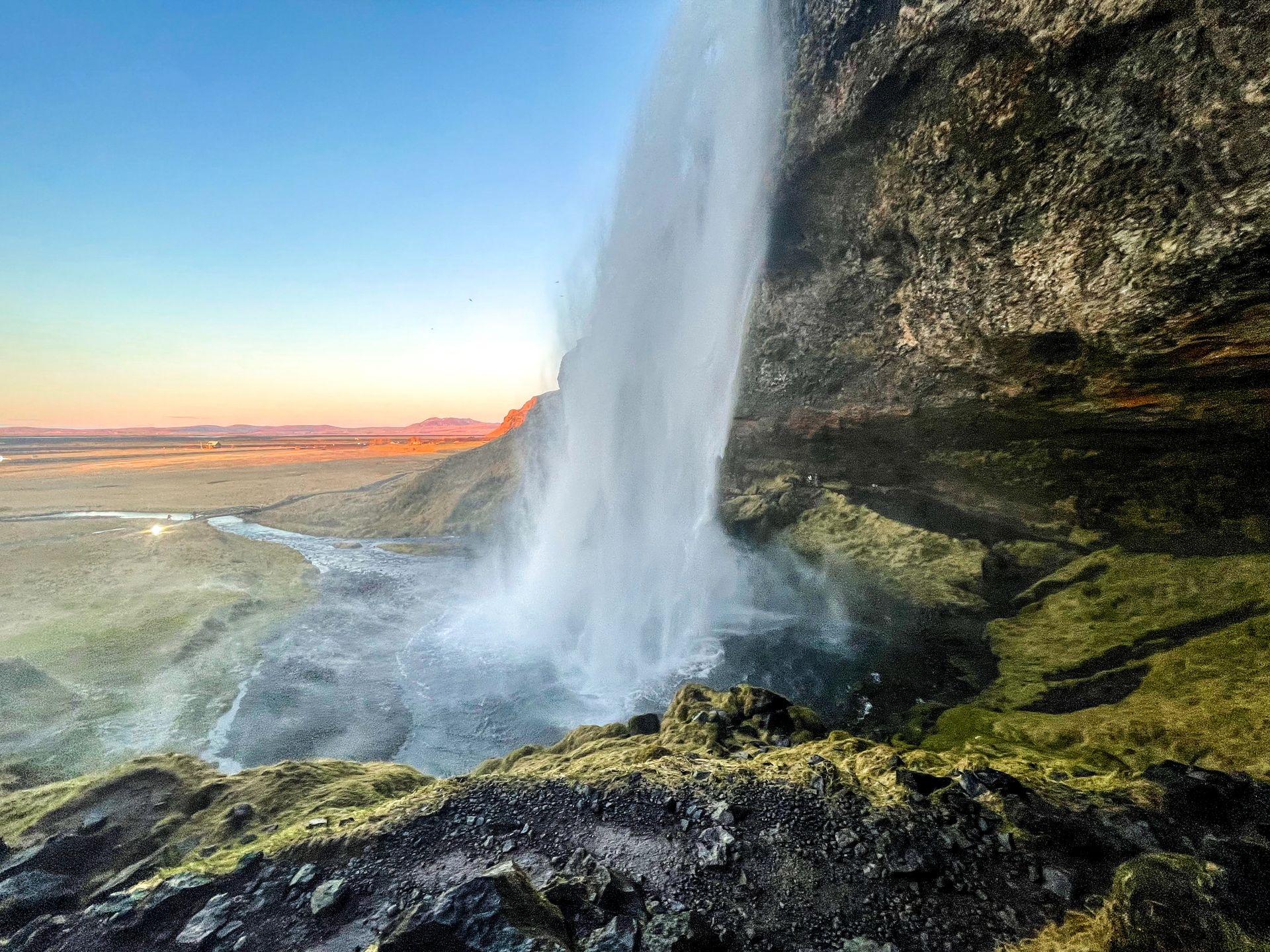 Looking at the side of Seljalandsfoss. The mountains in the distance are glowing orange with the setting sun.