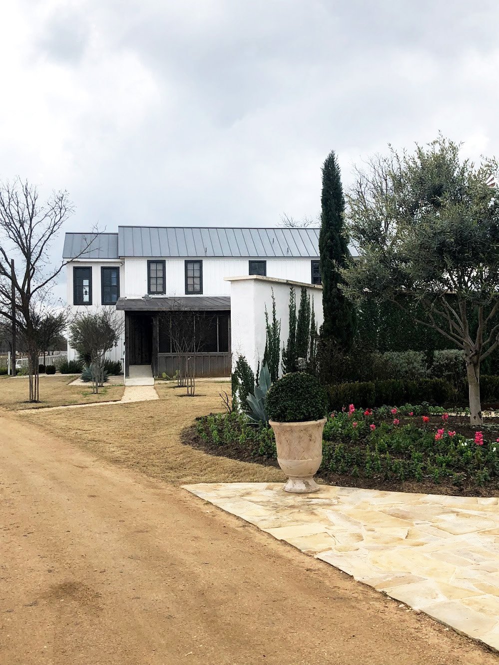 A white building with greens and well landscaped bushes in front.