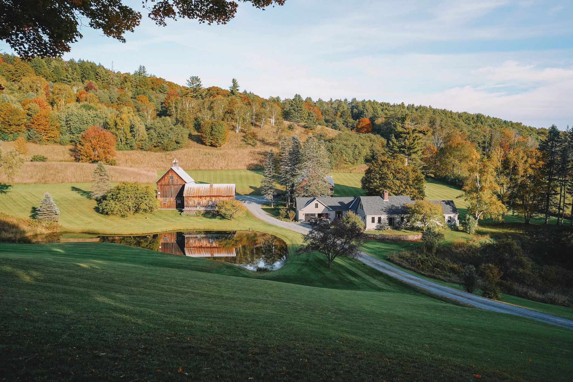 A farm that has a picturesque pond and two buildings.