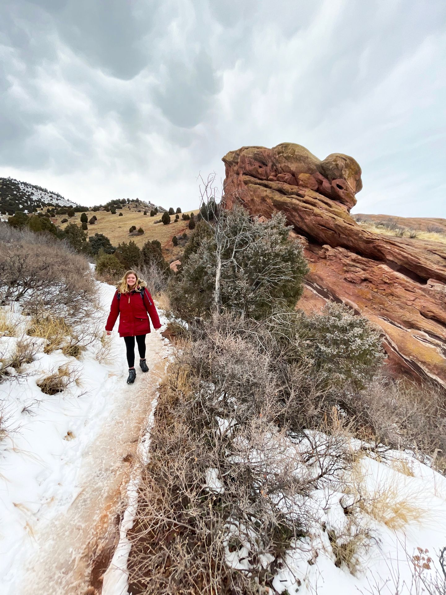 Lydia hiking on the Morrison Slide Trail. There is a round orange rock formation behind her.
