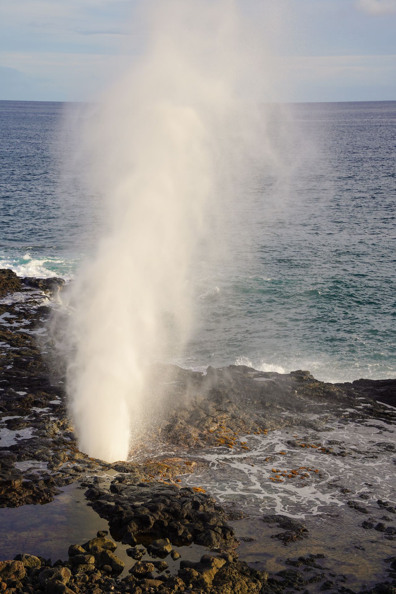 A white stream of water flying out of a rocky area at the Spouting Horn in Kauai