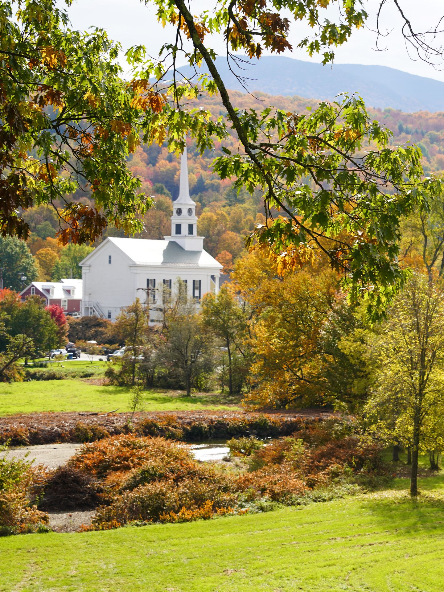 A white church with mountains in the background and trees in the foreground.