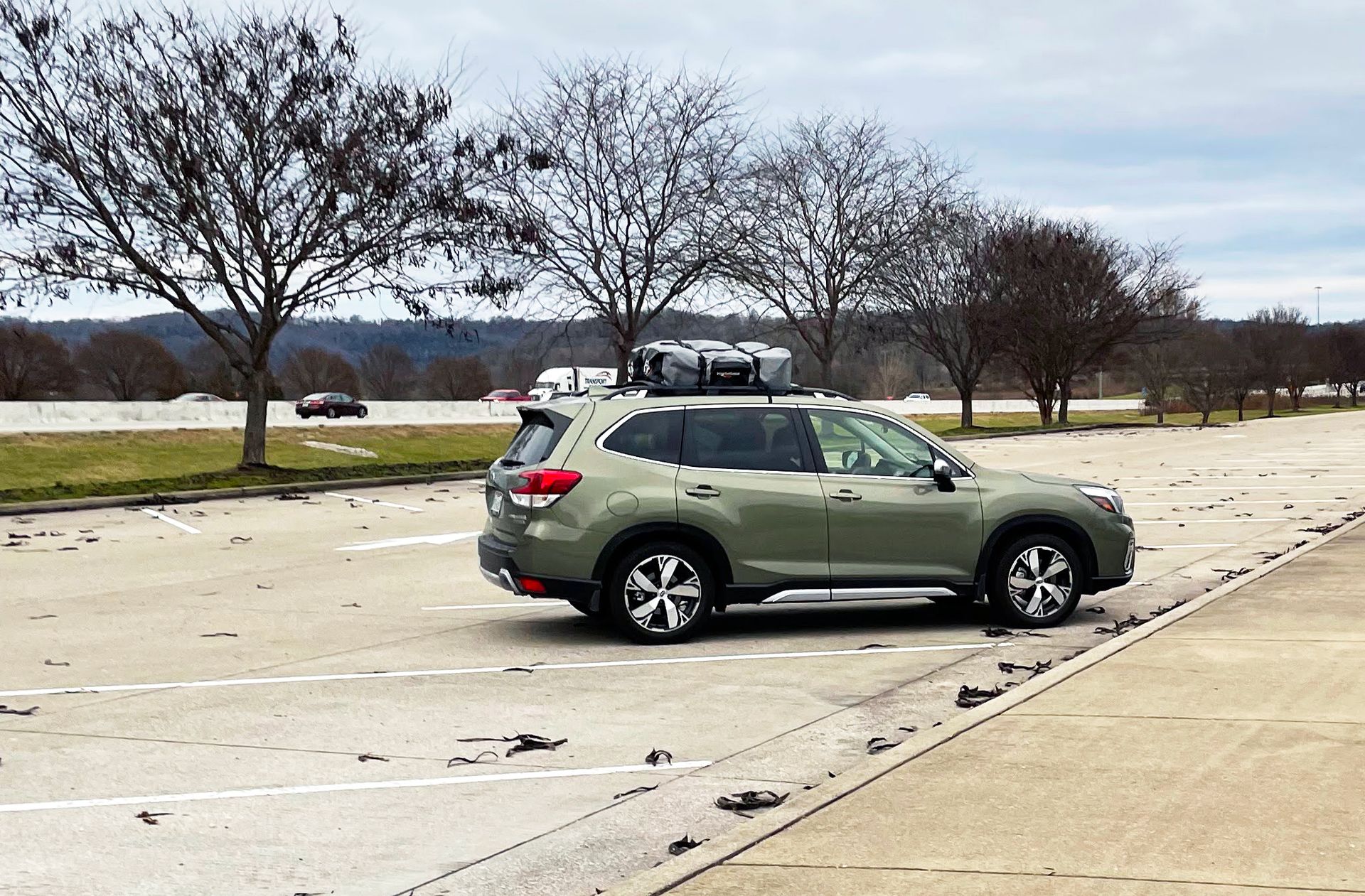 A green Suburu Forester with large duffel bags on the roof.