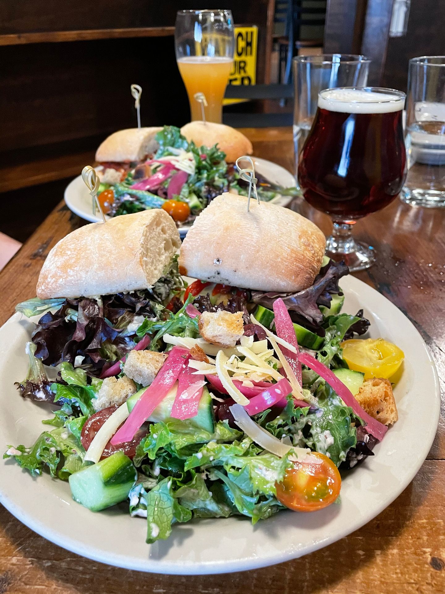 A plate full of greens with a sandwich on ciabatta bread.