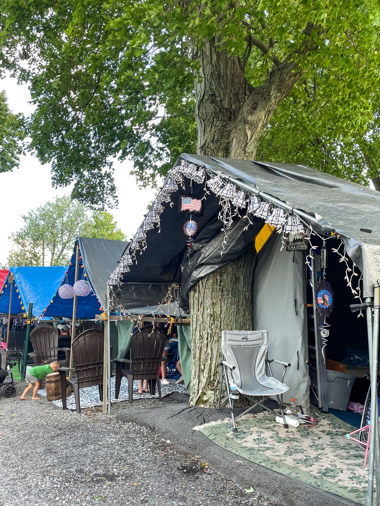 A row of canvas tents decorated with lights. The closest tent has a hole to allow for a giant tree.