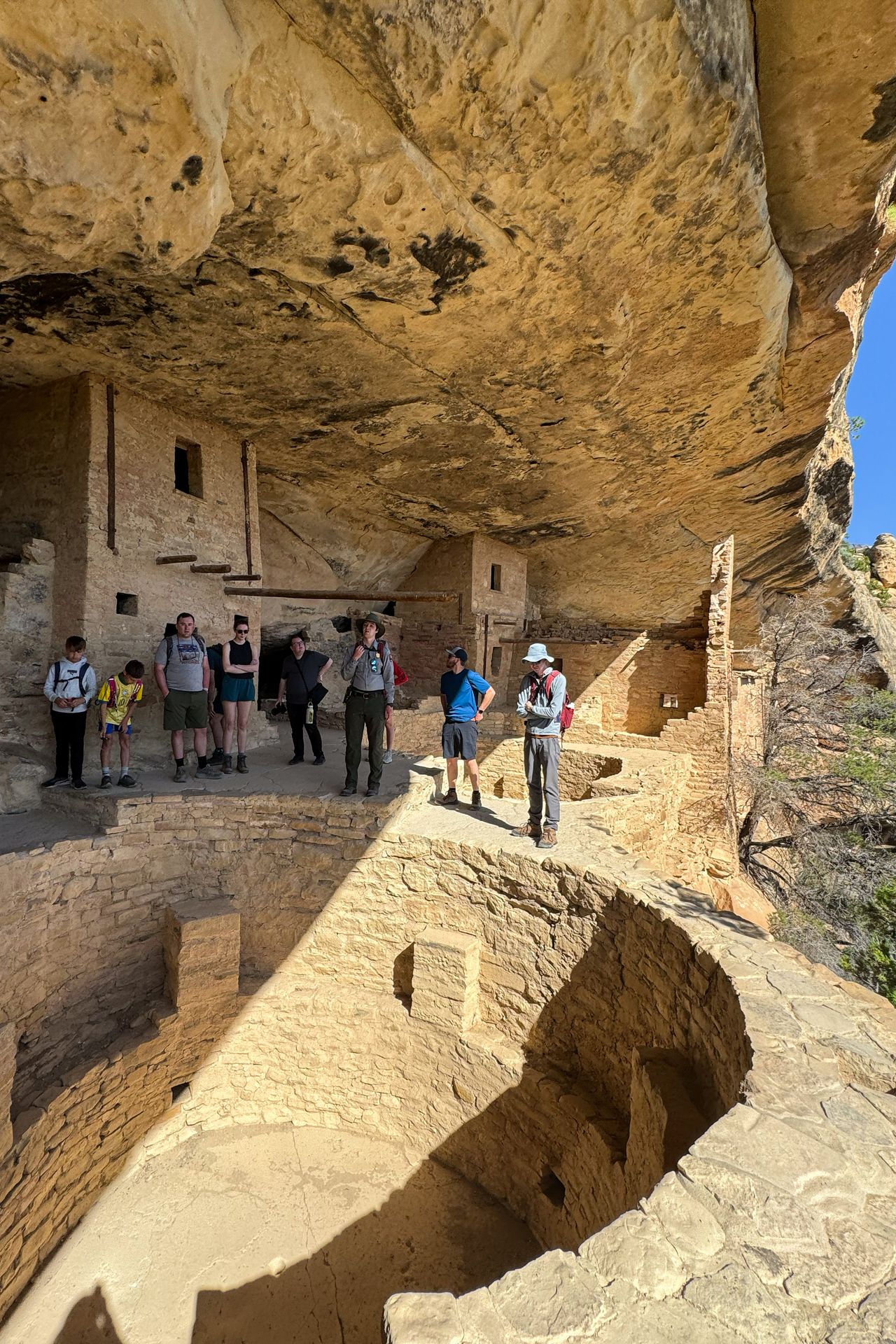 A line of people standing above a kiva inside of Balcony House