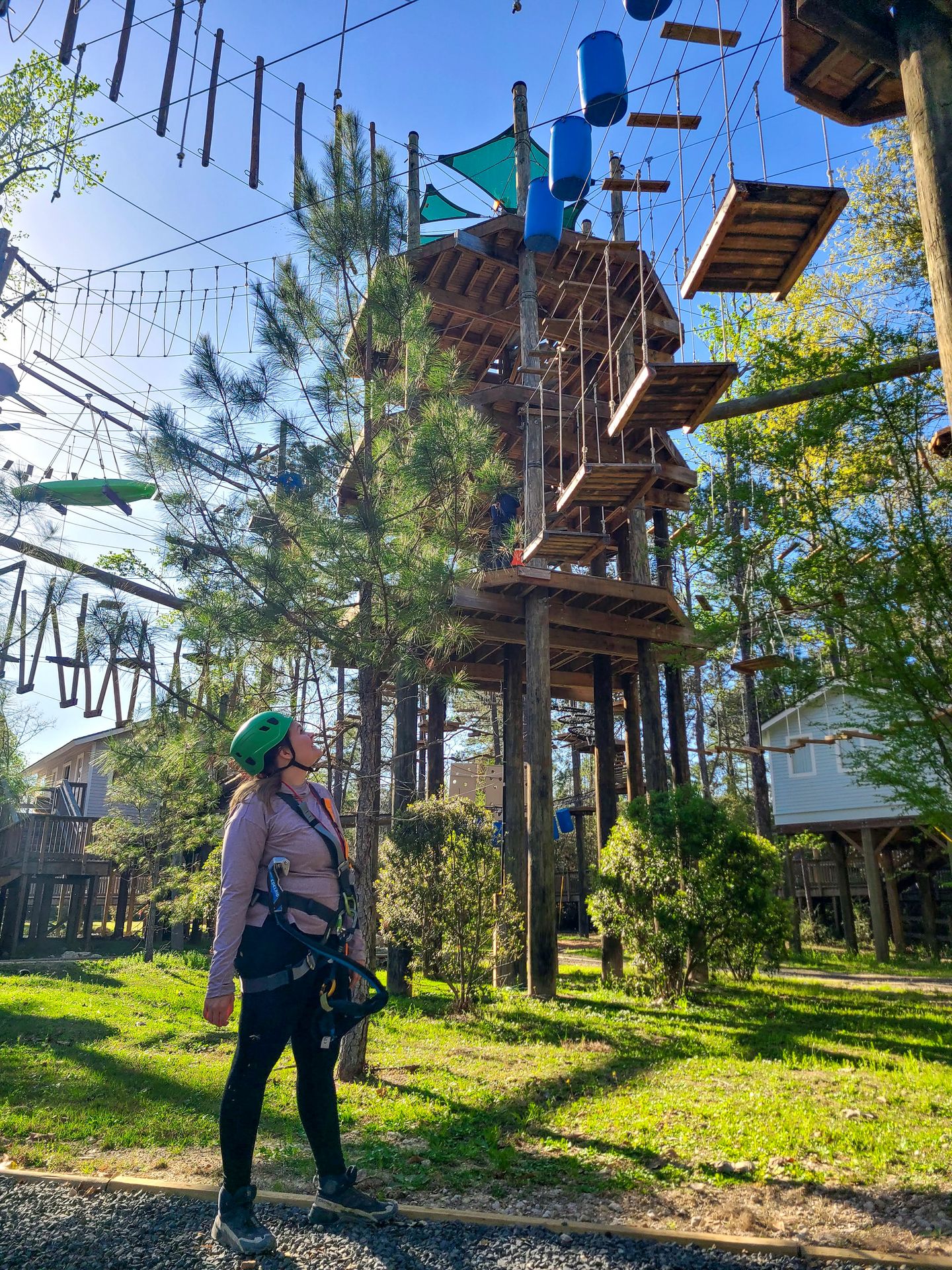 Lydia looking up at the Texas TreeVentures rope course wearing a harness and helmet.