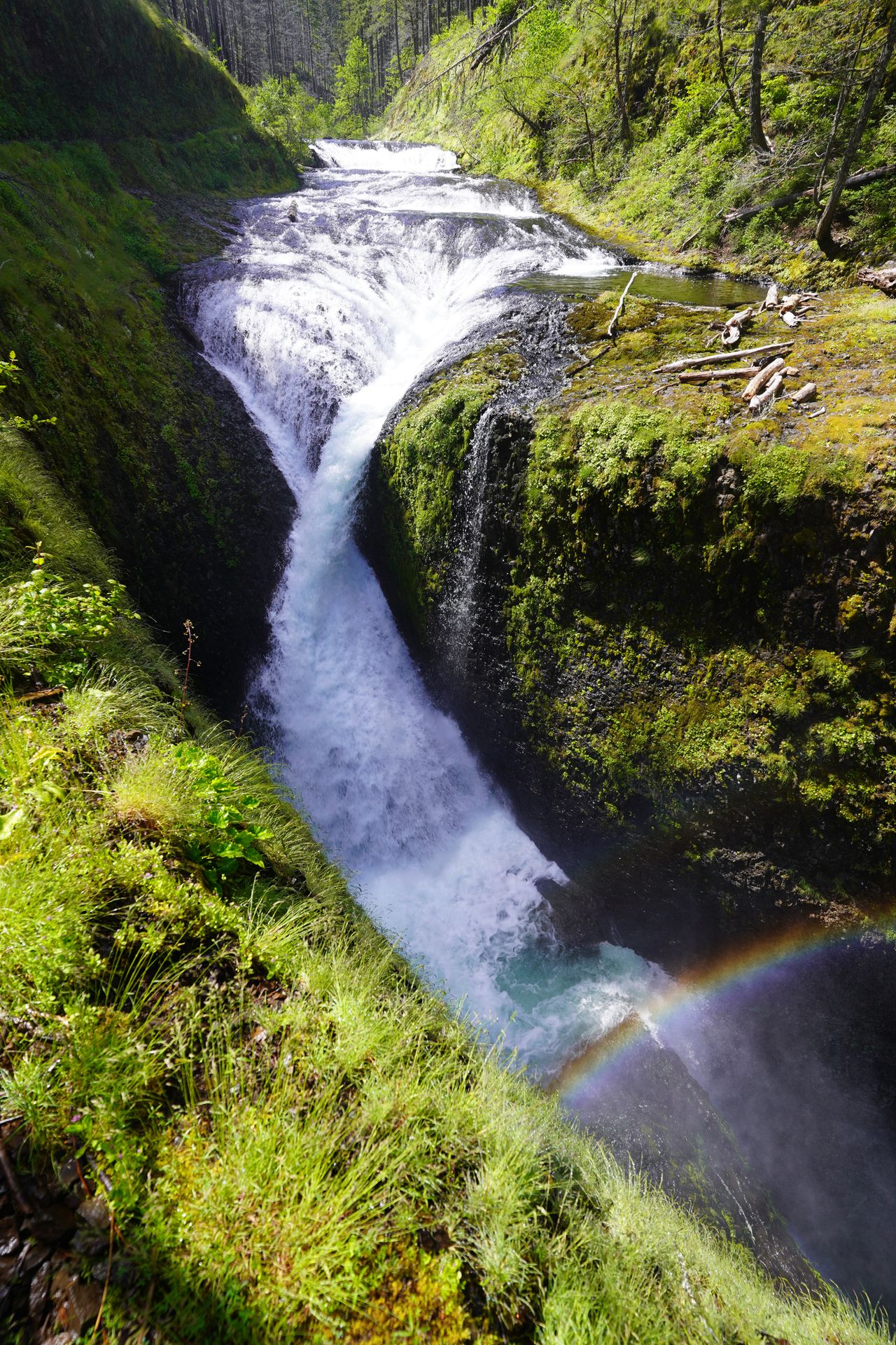 A waterfall that looks like it twists and a rainbow above it